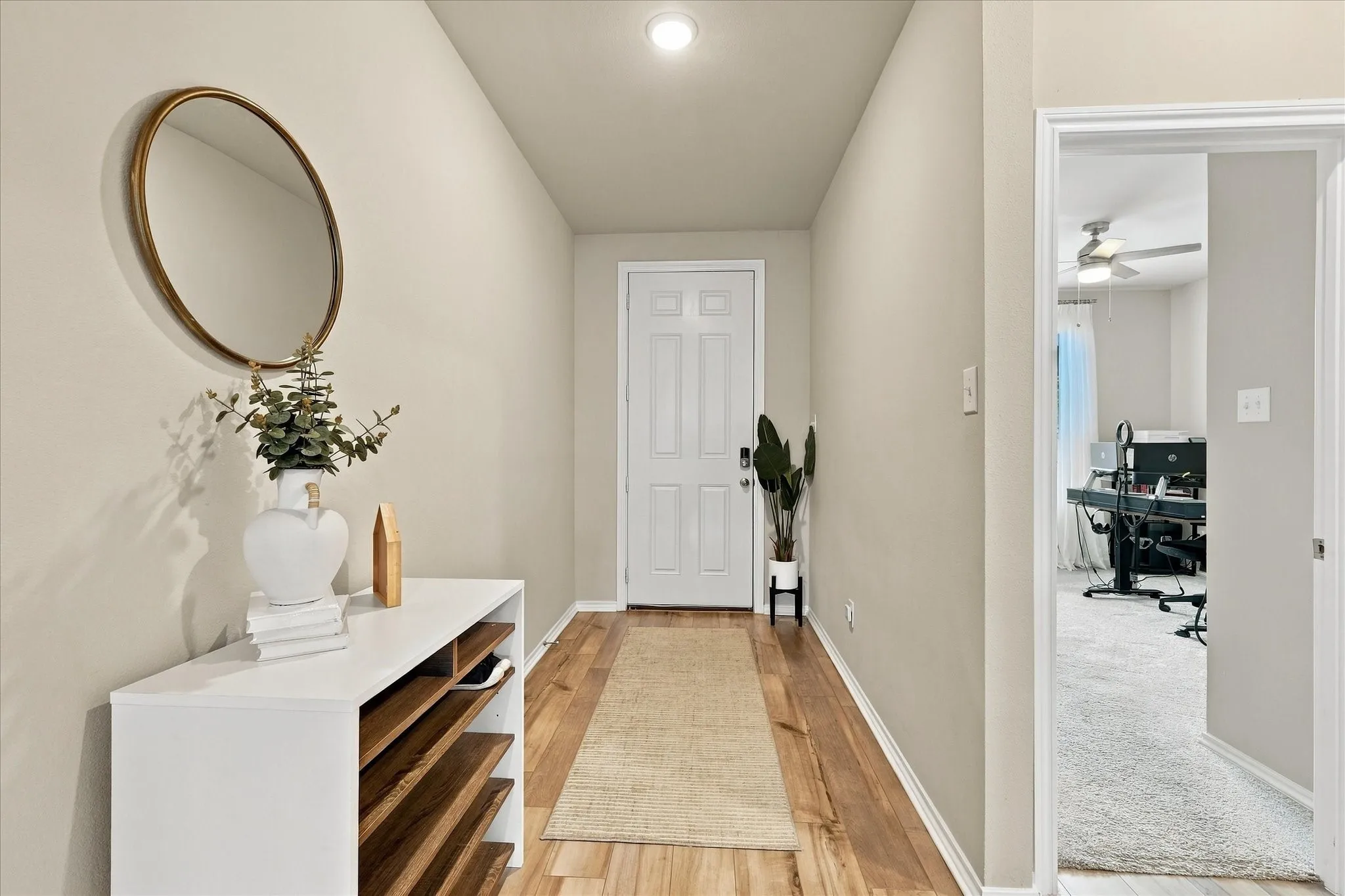 Recessed ceiling lighting, wood-finish flooring, light neutral wall tones, white interior door with paneling, and an open doorway to another room