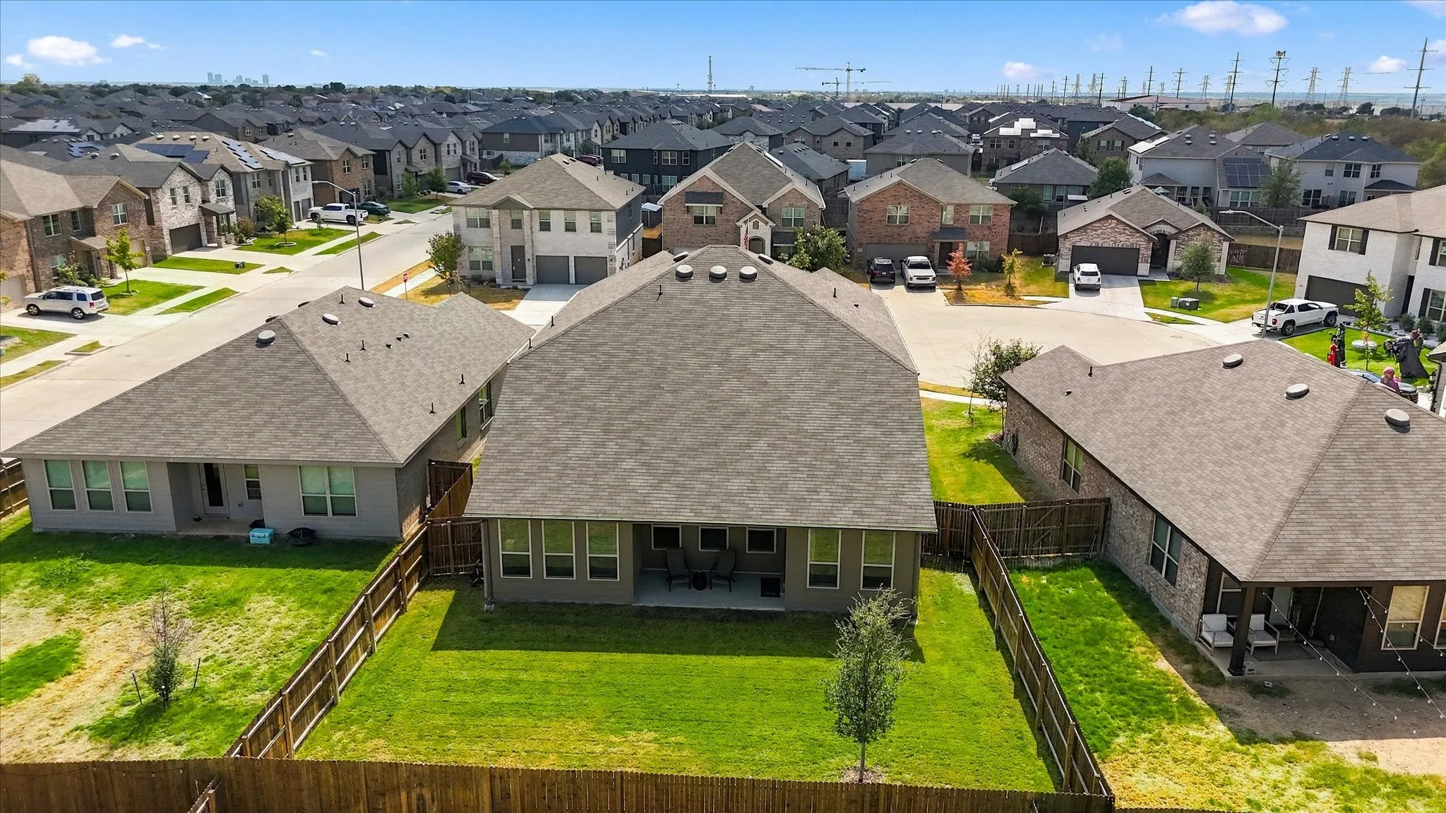 Expansive fenced backyard with a manicured lawn, established tree, and covered patio
