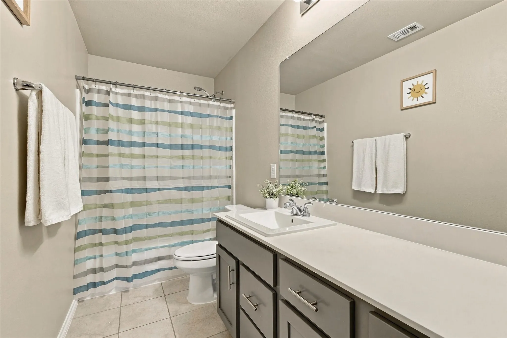 Bathroom featuring a single vanity with a white countertop, chrome fixtures, built-in cabinetry with brushed nickel pulls, a shower-tub combination, and tiled flooring