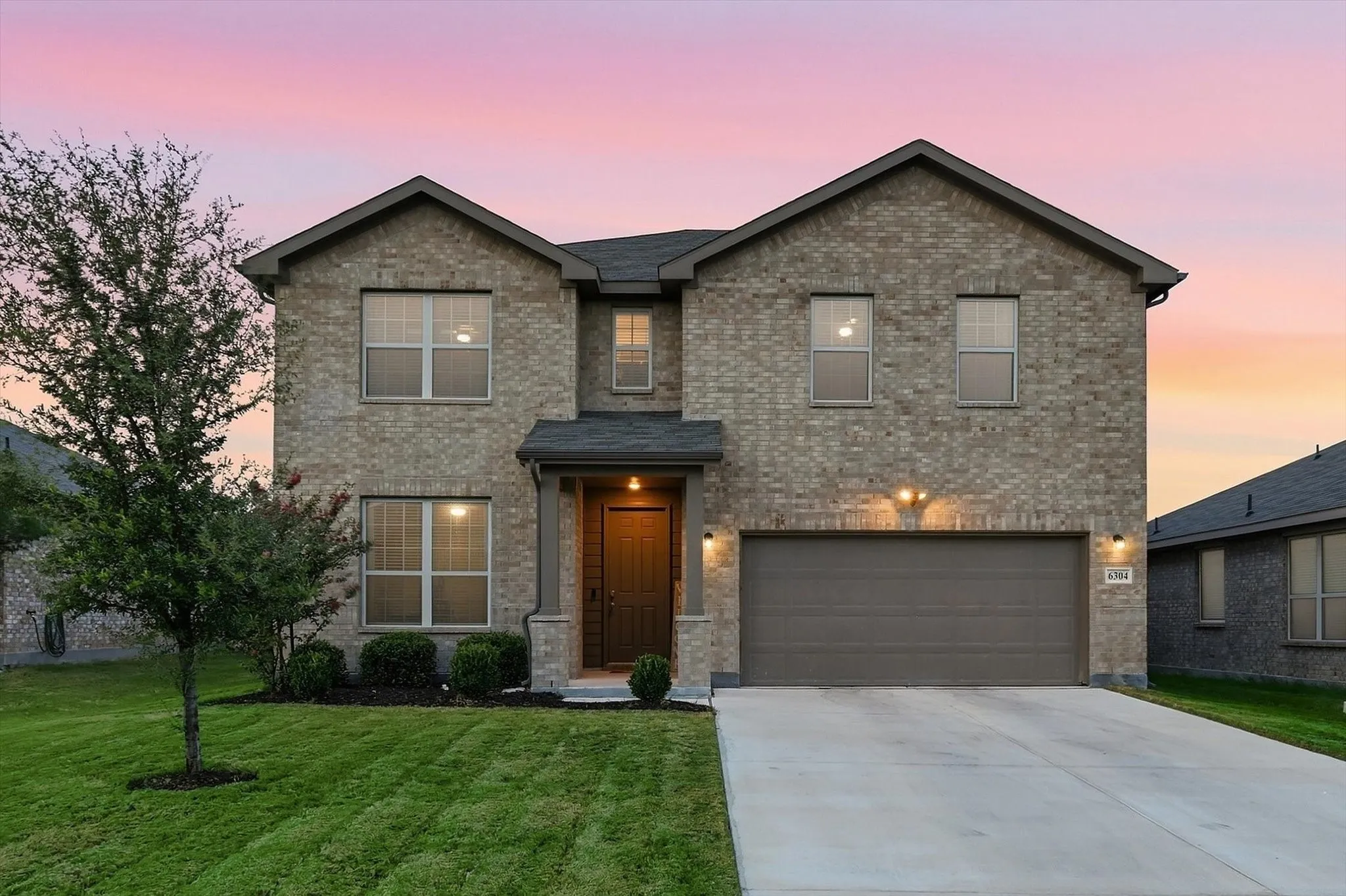 Two-story brick exterior with a gabled roofline, attached two-car garage, concrete driveway, and a covered entry with stone columns