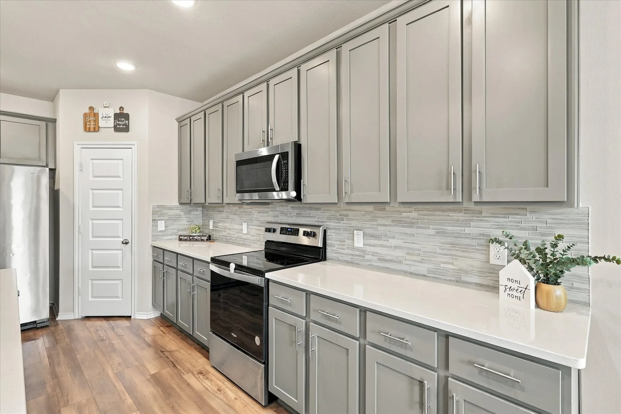 Wood-finish flooring, light gray cabinetry, stainless steel appliances, white countertops, and a full-height tile backsplash