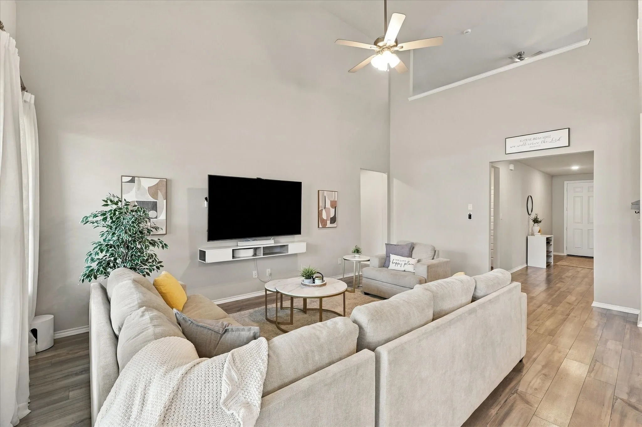 Vaulted ceiling with a ceiling fan, wall-mounted media console, and wood-finish flooring