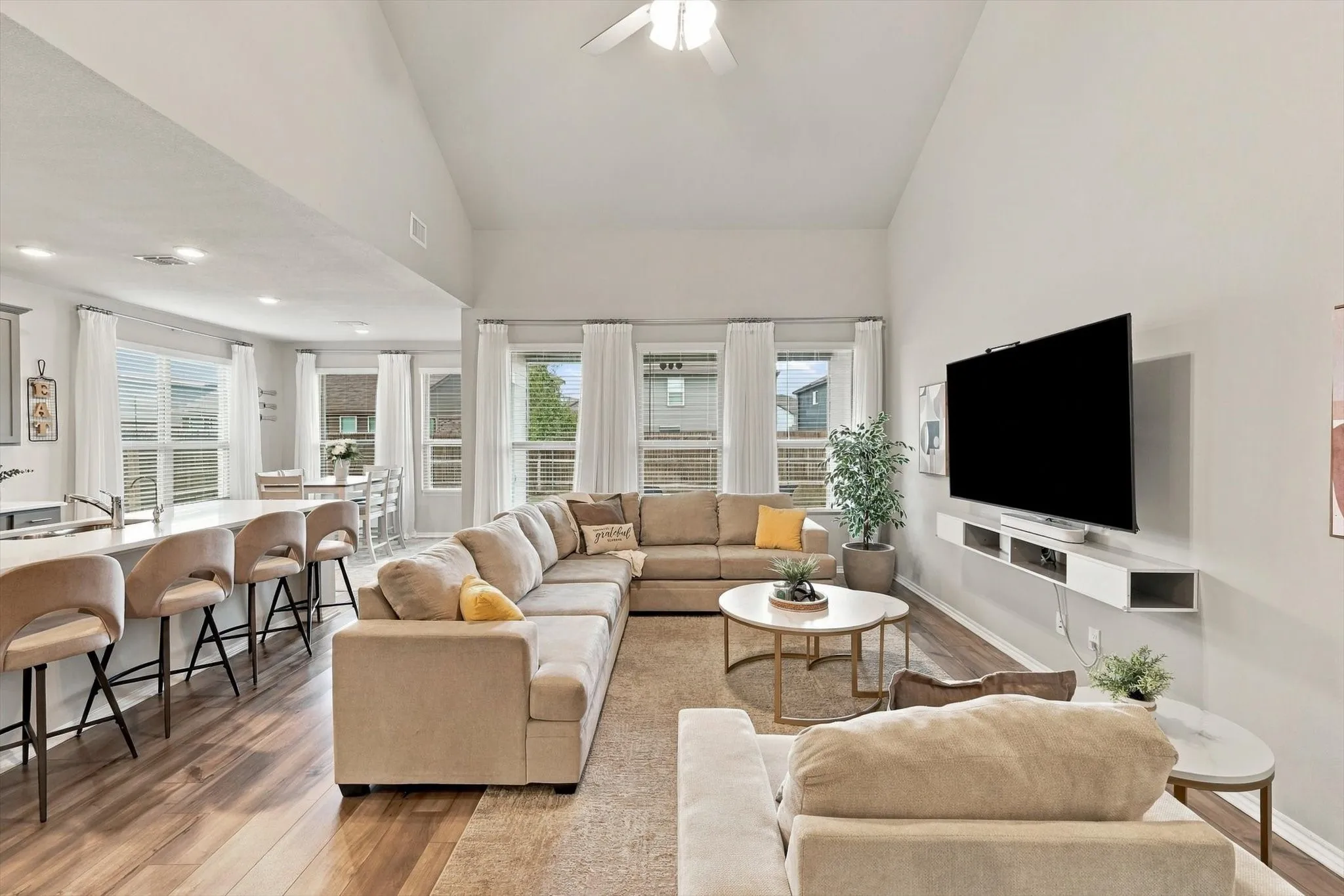 Open-concept living area featuring vaulted ceilings, wood-finish flooring, a kitchen island with seating, and multiple large windows