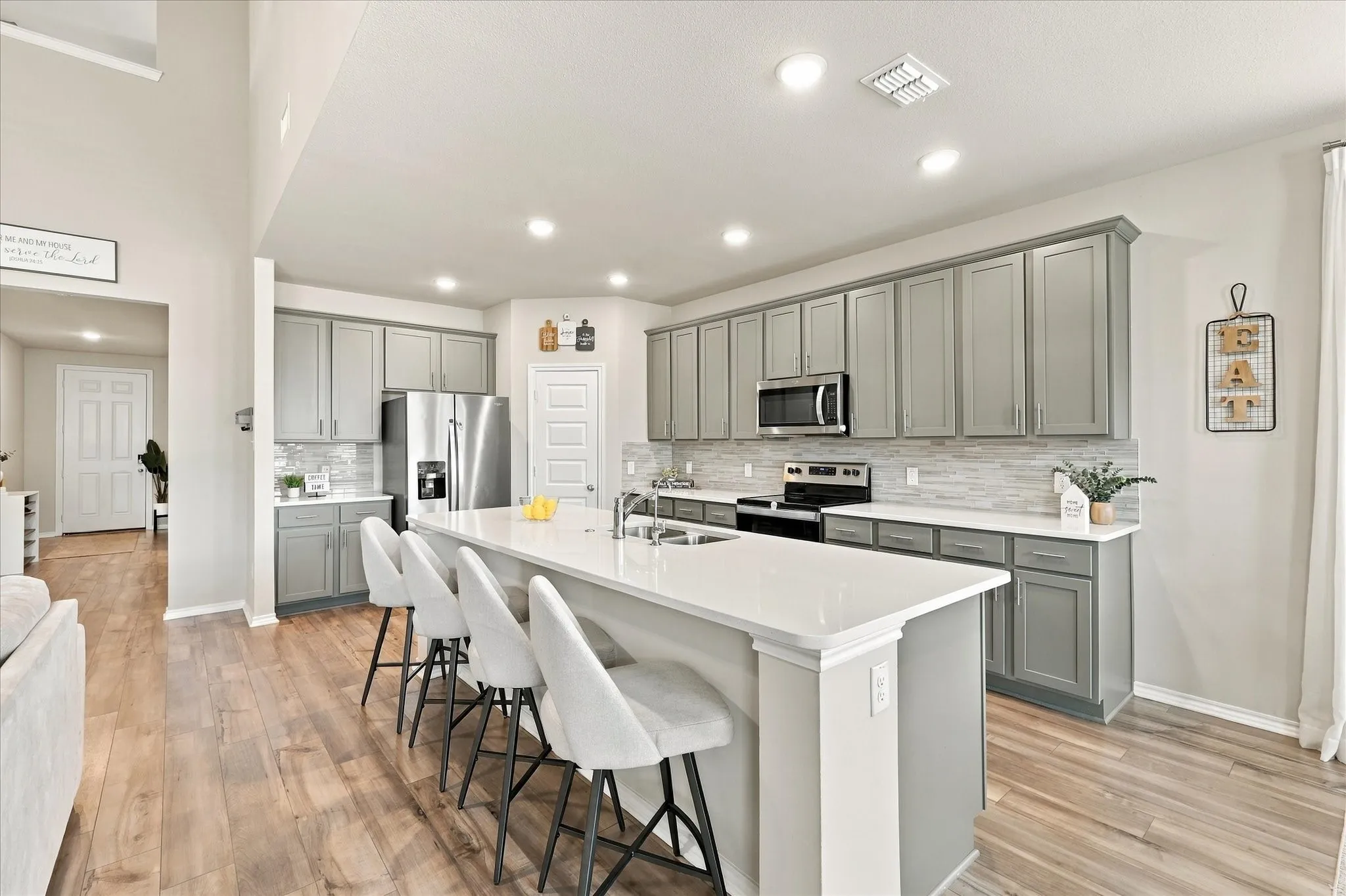 Kitchen featuring a large island with white countertop, recessed lighting, wood-finish flooring, and gray cabinetry with stainless steel appliances