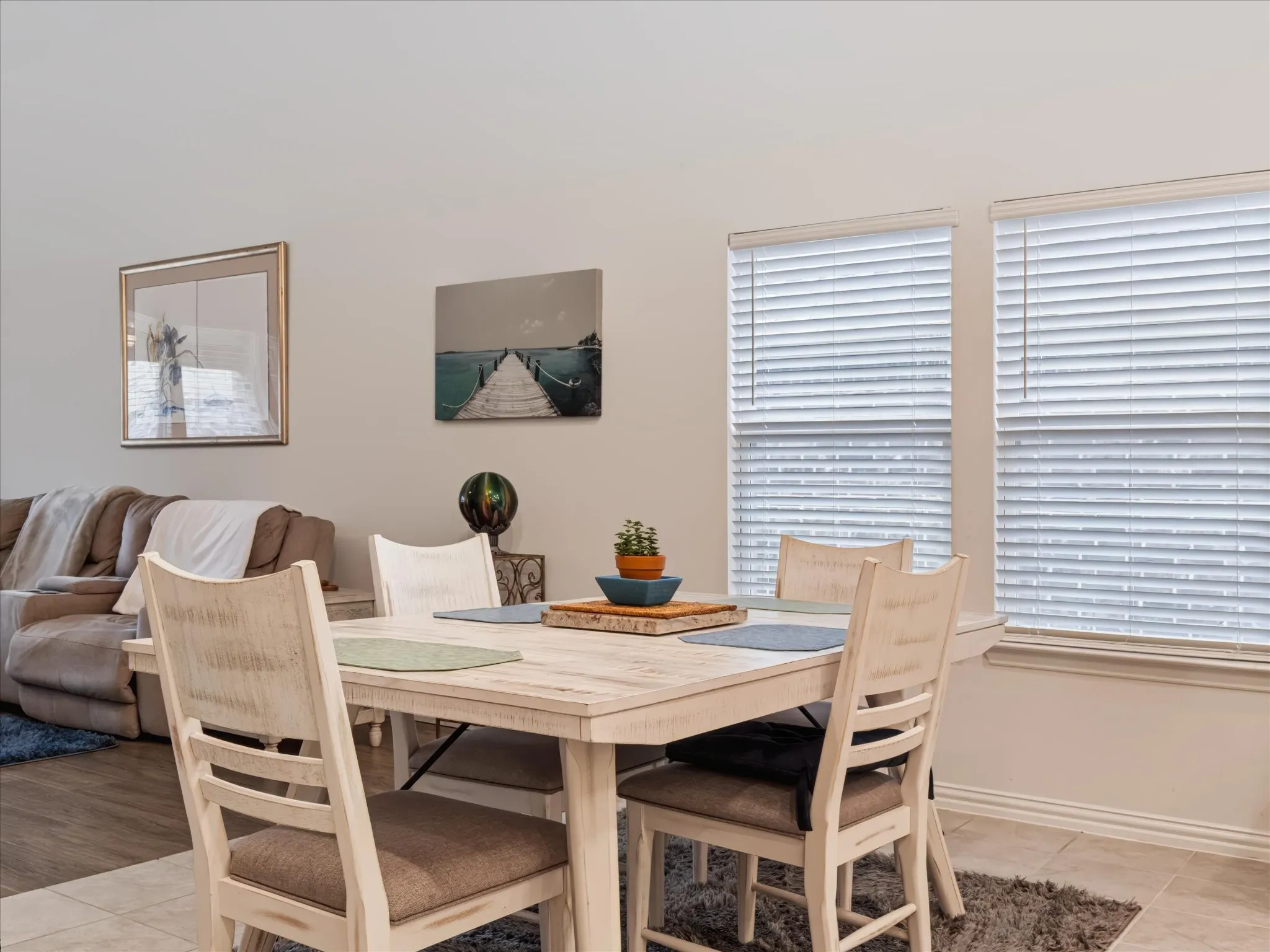 Two large windows with blinds, light tile flooring, and light wall finishes create a bright atmosphere