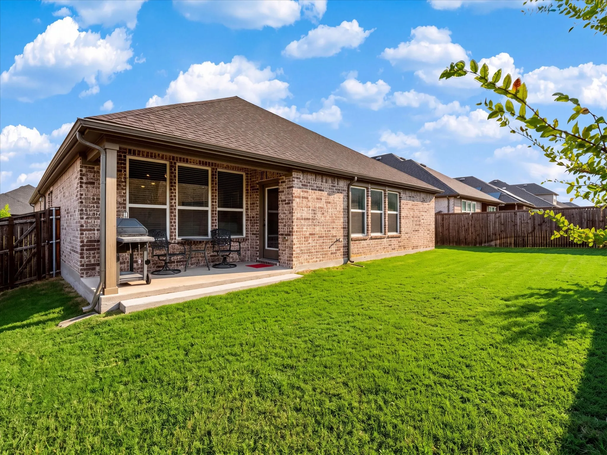 Brick exterior, covered patio, privacy fence, green lawn, multi-pane windows.  Digitally enhanced to show green grass.