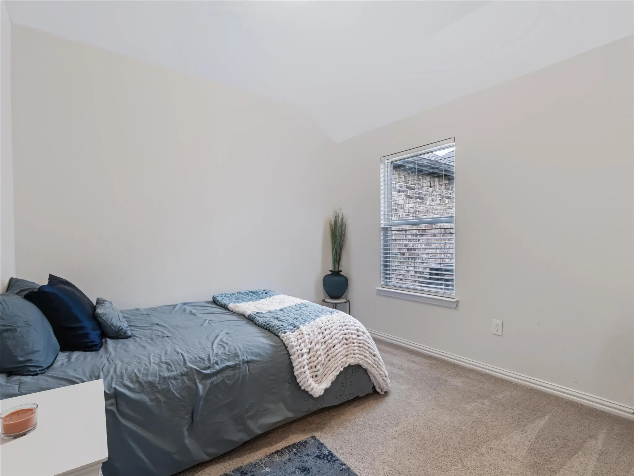 Carpeted flooring, vaulted ceiling, single window with blinds, and neutral wall tones