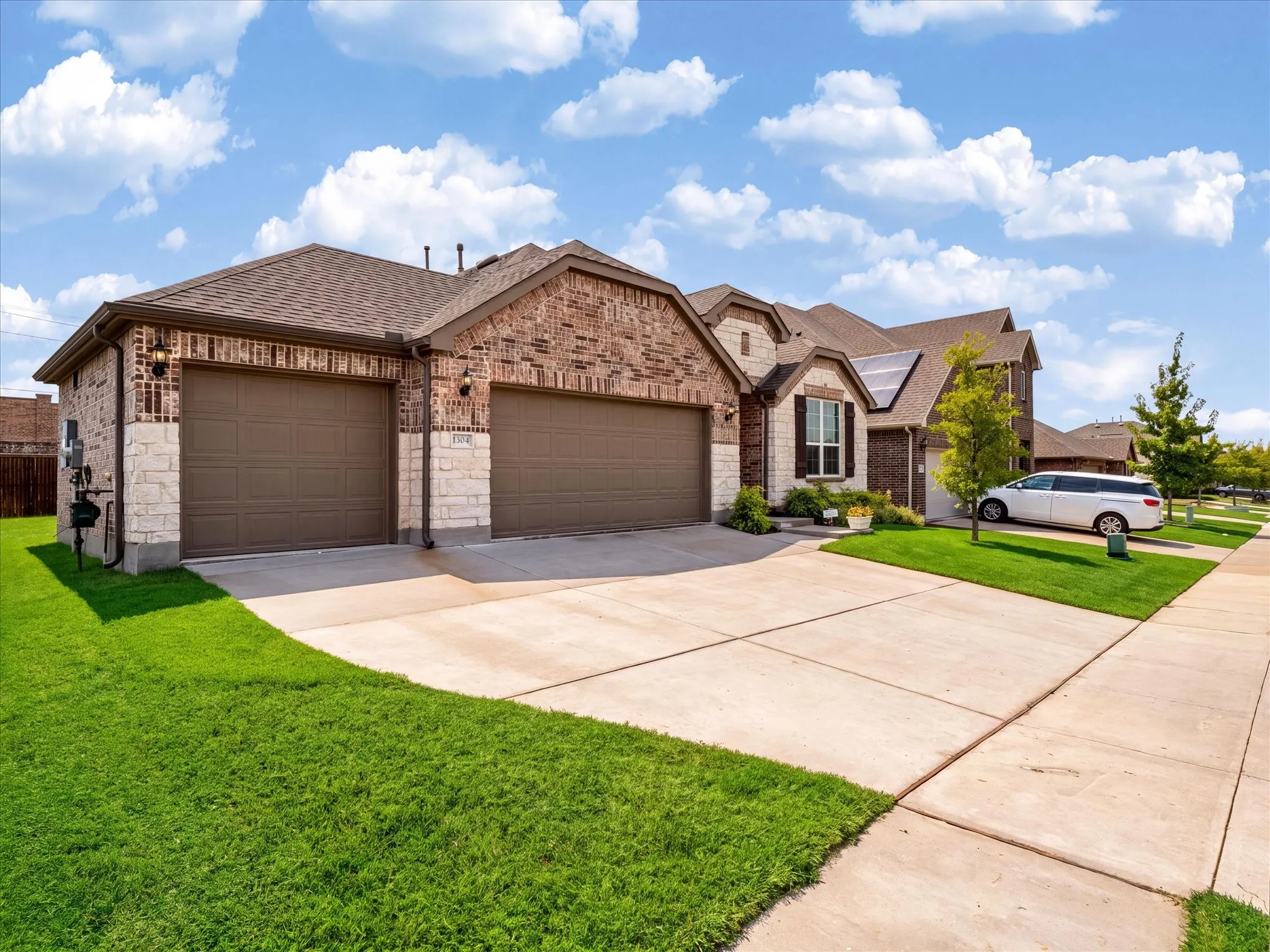 Brick and stone facade with dark brown garage doors.  Digitally enhanced to show green grass.