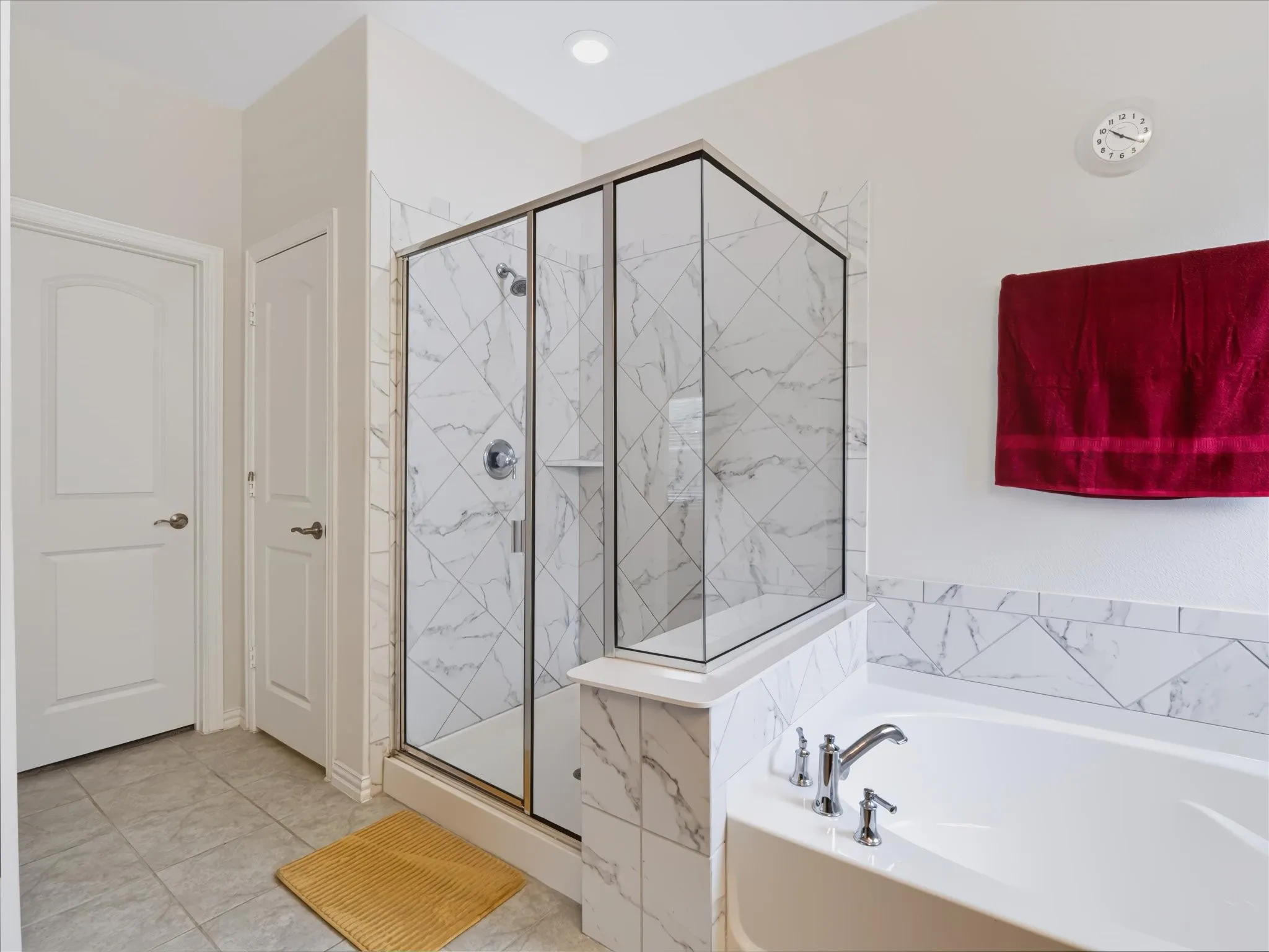 Glass-enclosed shower with white marble-look tile, deep soaking tub with chrome fixtures, and light gray floor tiling