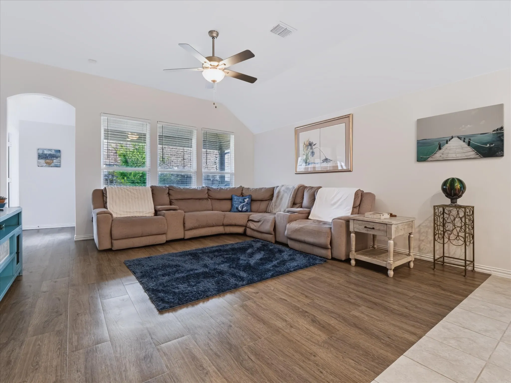 Vaulted ceiling, wood-finish flooring, ceiling fan with integrated lighting, arched doorway, and multiple windows