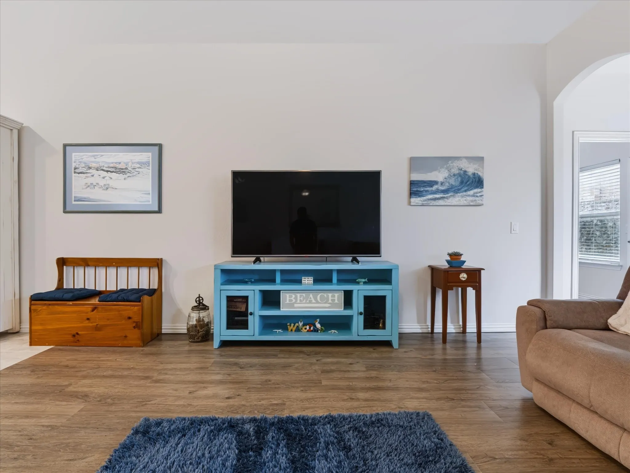 Spacious living room featuring hardwood flooring, a blue media console with open shelving, and an arched architectural detail