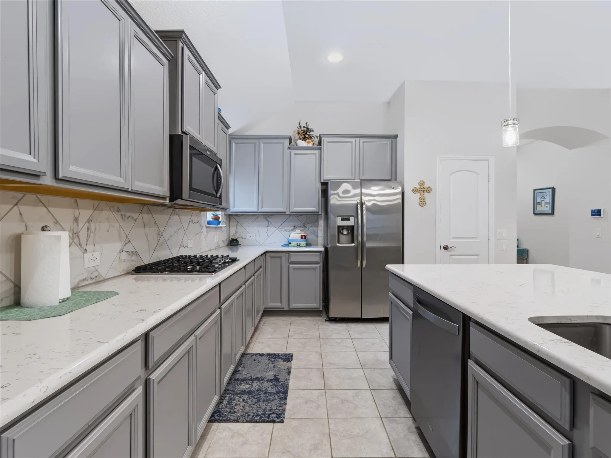 Grey shaker-style cabinetry, stainless steel appliances, light-toned countertops, geometric pattern backsplash, and tile flooring