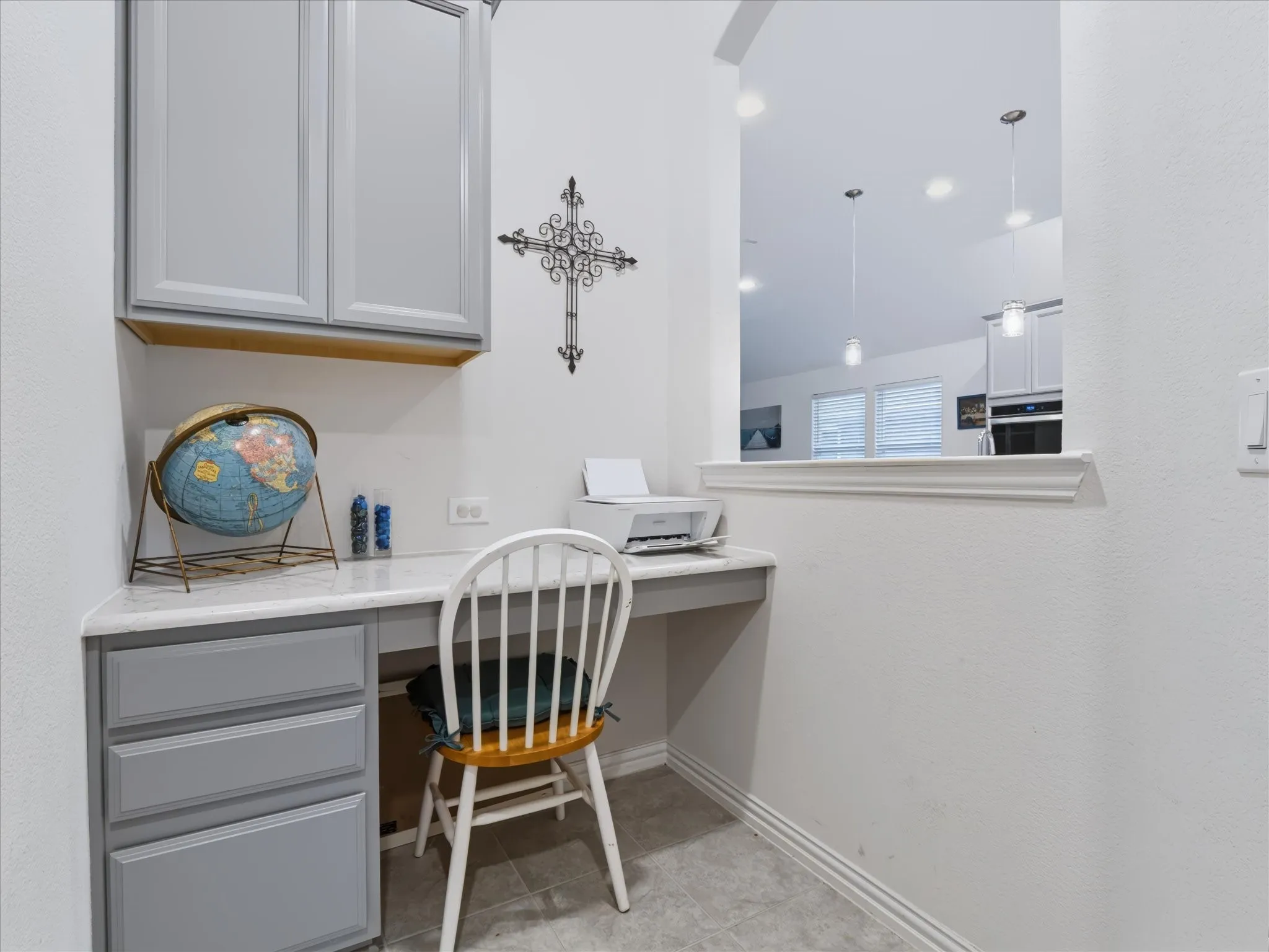 Built-in desk with light gray cabinetry and white countertop, featuring an overhead cabinet and a pass-through window with trim detail