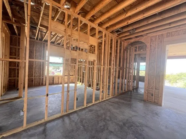 Open framing construction with exposed ceiling joists, concrete slab foundation, and an arched doorway. Looking from the living room toward the primary bedroom