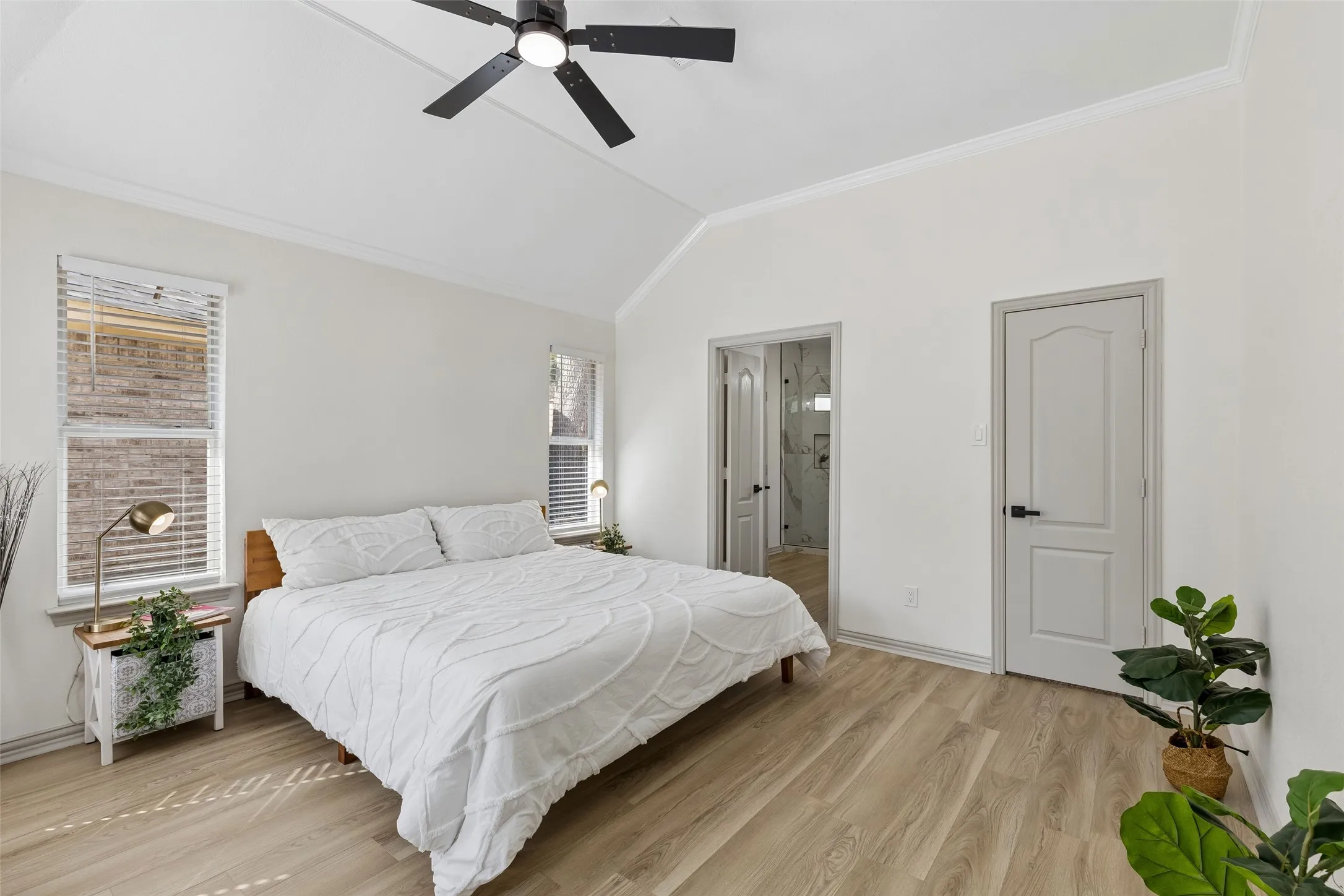 Vaulted ceiling with a ceiling fan, crown molding, wood-finish flooring, white paneled doors, and dual windows