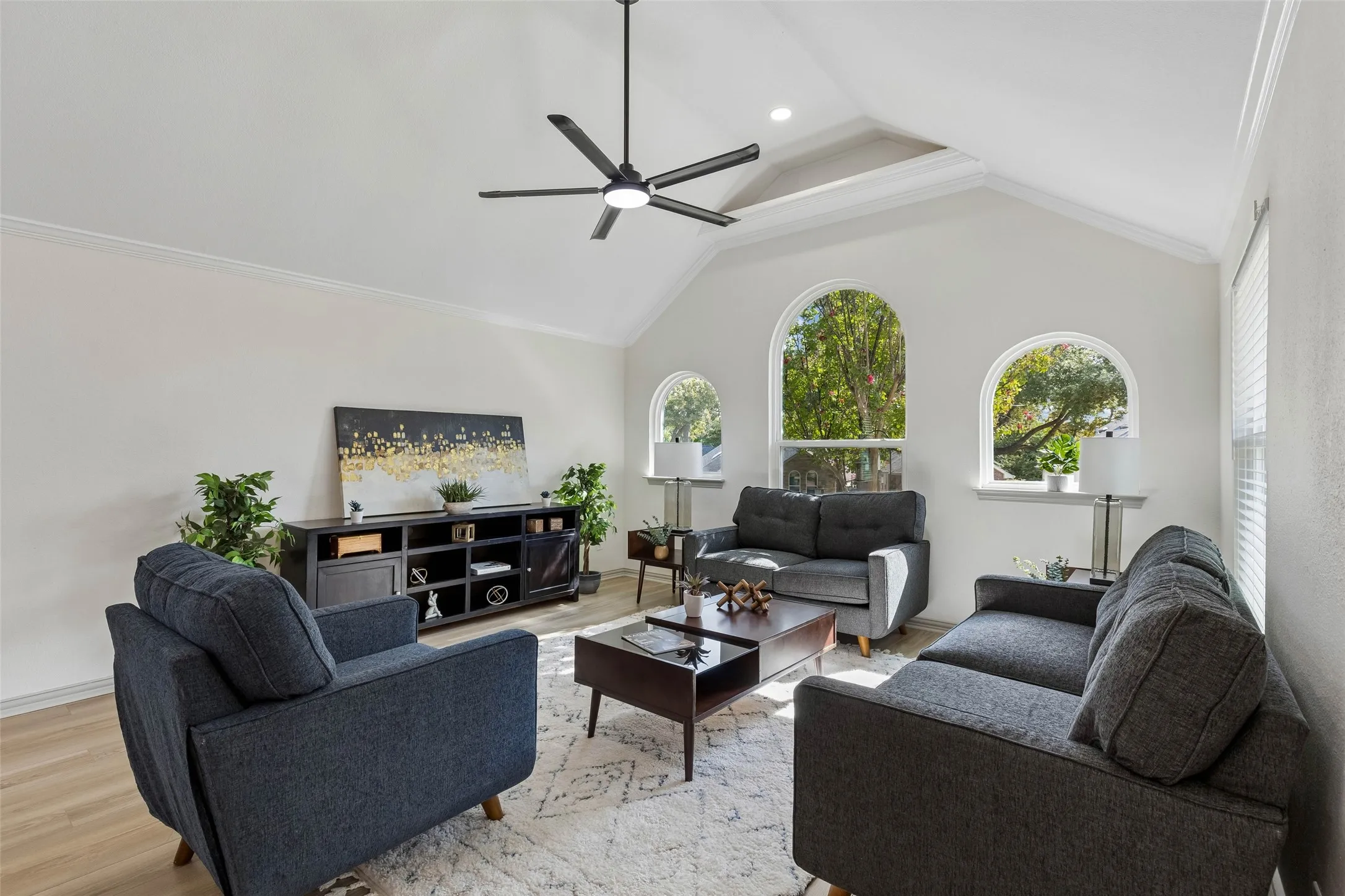 Vaulted ceiling with a contemporary ceiling fan, multiple arched windows, crown molding, and wood-finish flooring