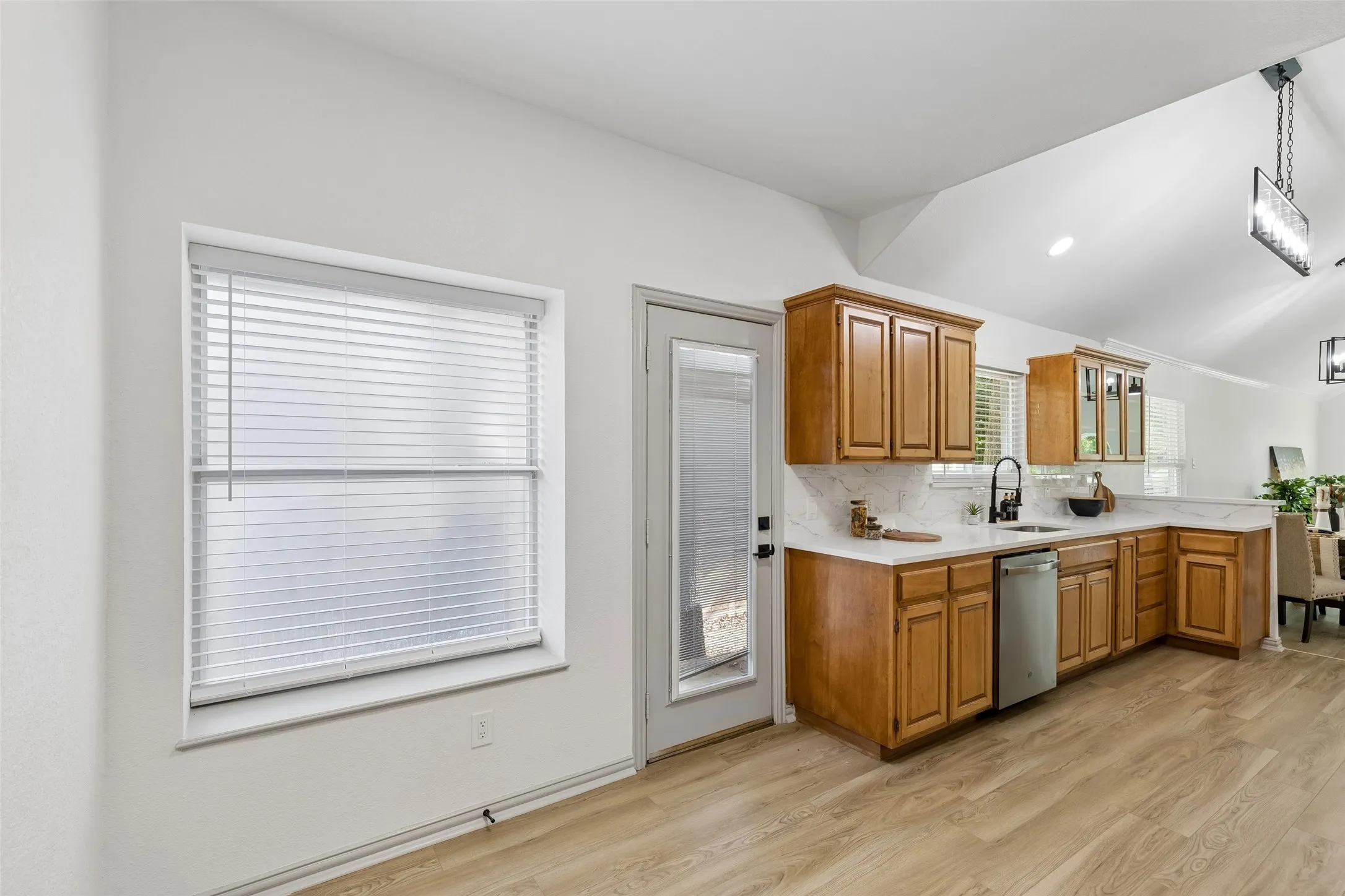 Kitchen featuring wood cabinetry, light-toned countertops, a stainless steel dishwasher, and a black sink fixture