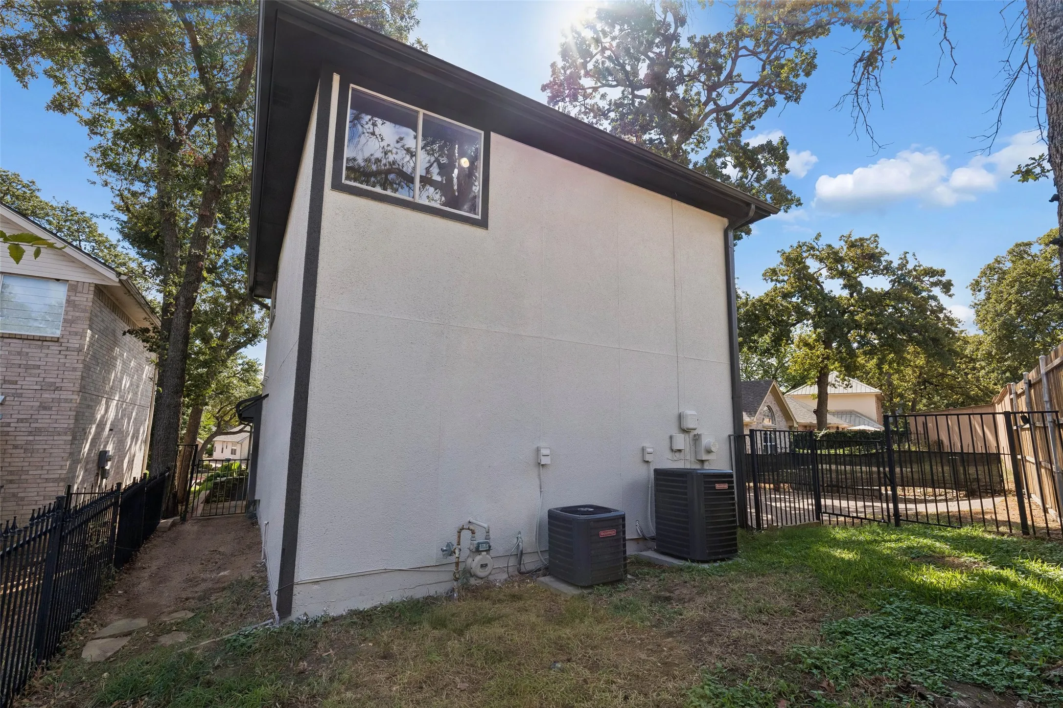 Exterior wall with white stucco finish and dark trim, featuring a single window and two external AC units