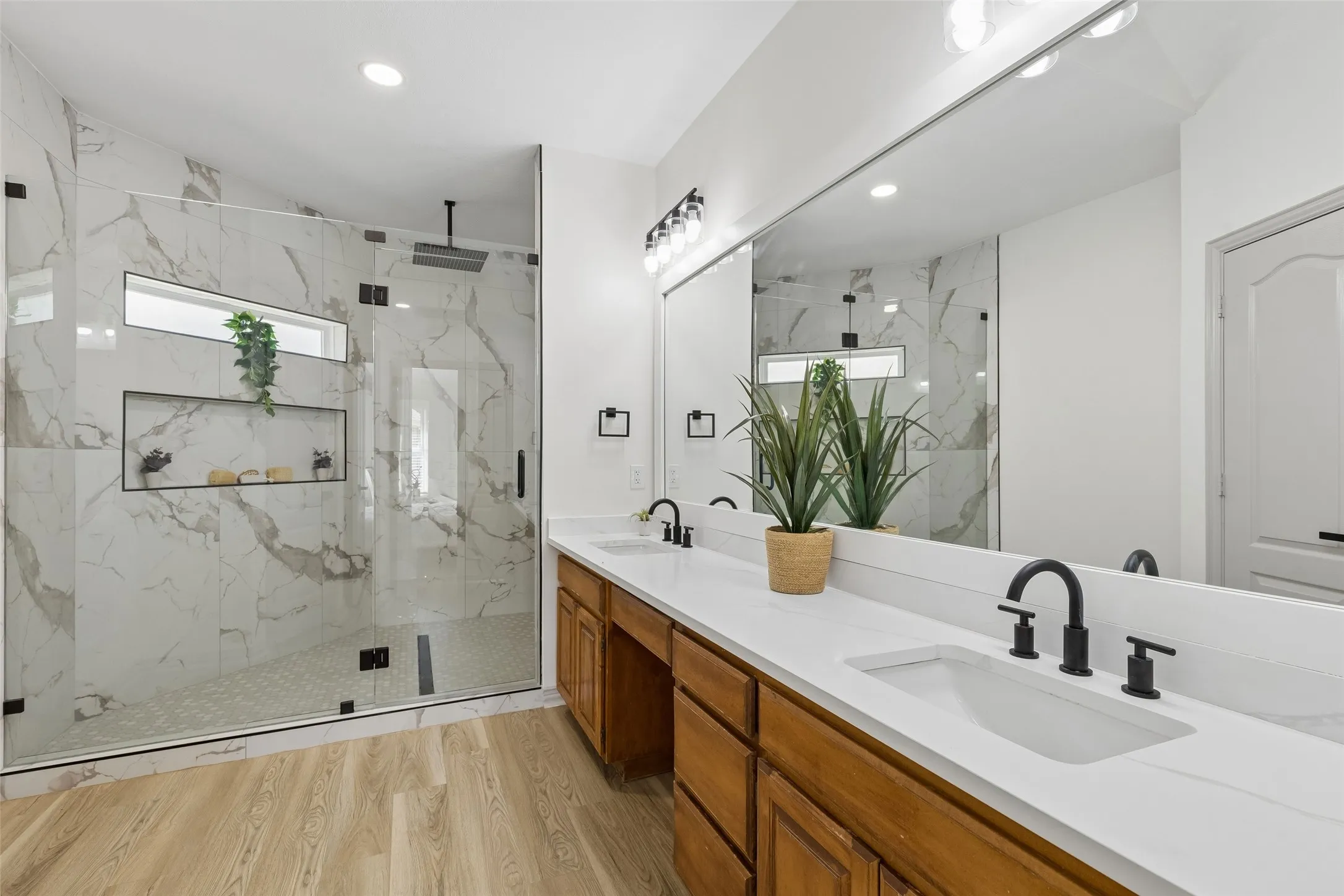 Spacious bathroom featuring a dual vanity with white countertops, wood-finish cabinetry, and black fixtures