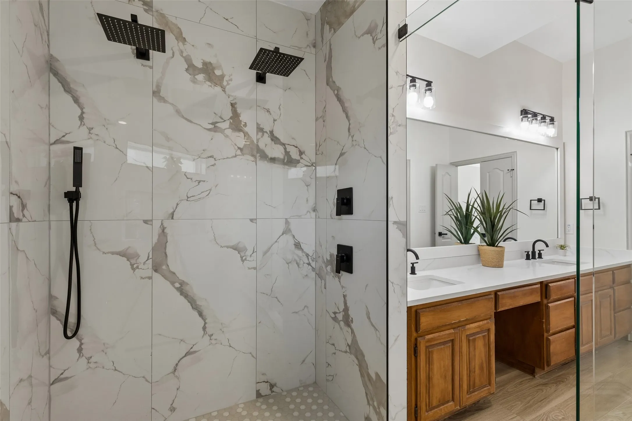 Walk-in shower with dual matte black rainfall showerheads and a handheld sprayer