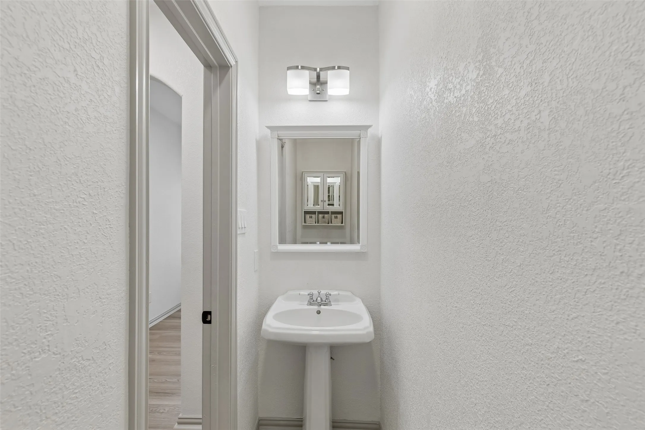 Pedestal sink with chrome faucet, framed mirror, and dual-light vanity fixture