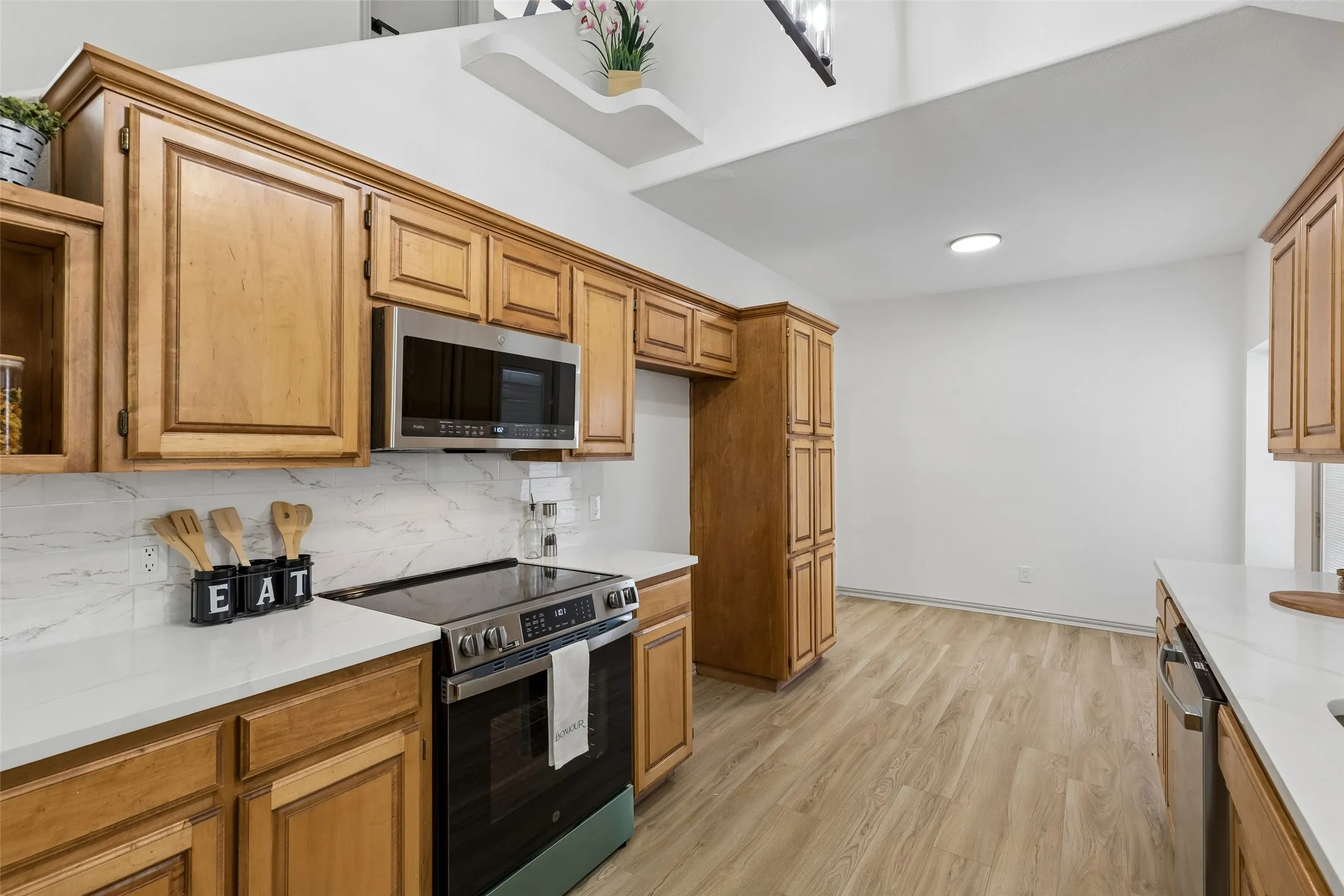 Wood-finish flooring, wood cabinetry, stainless steel appliances, white countertops, and a white tile backsplash