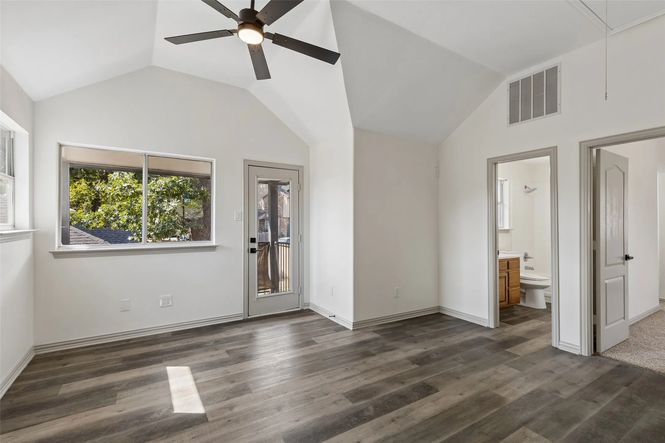 Vaulted ceiling with a ceiling fan, wood-finish flooring, a window with exterior scenery, a glass-paned door, and white walls