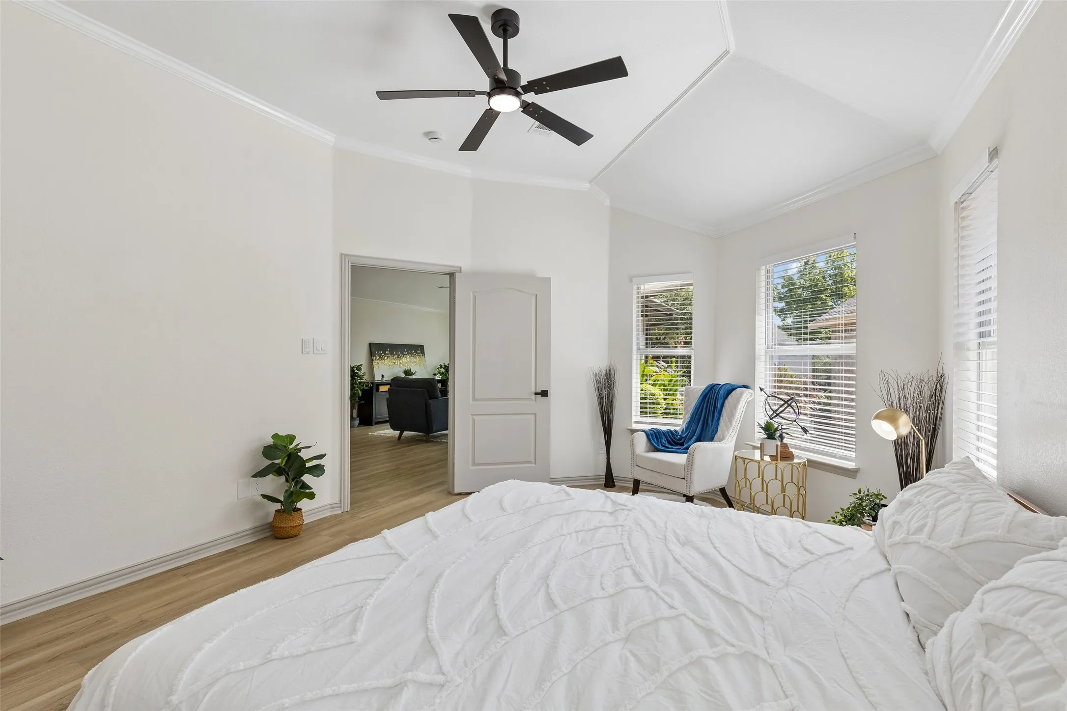 Vaulted ceiling with crown molding, wood-finish flooring, and multiple windows with blinds