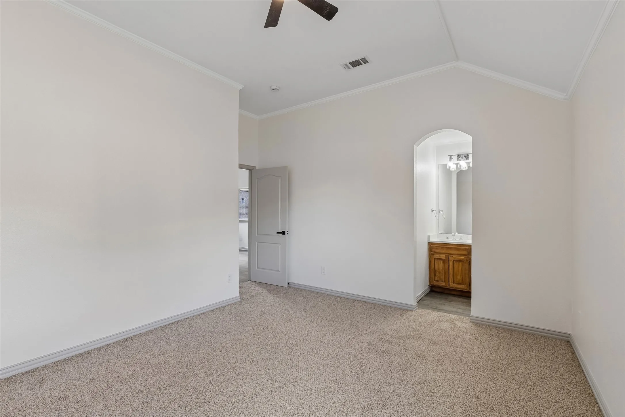 Vaulted ceiling, carpet flooring, arched doorway, wood-finish vanity, and ceiling fan