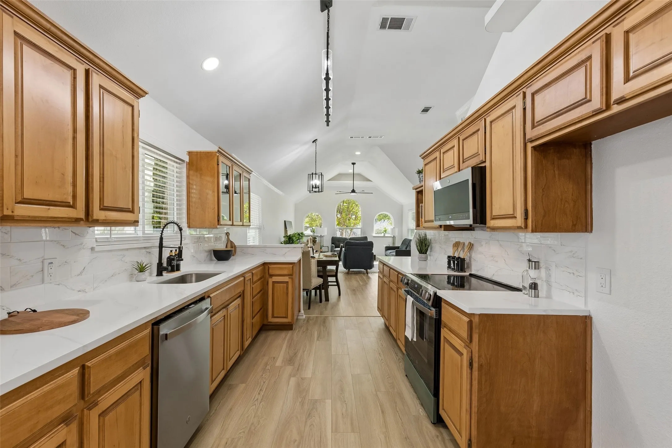 Kitchen featuring light wood cabinetry, white countertops, stainless steel appliances, a white tile backsplash, and light wood-finish flooring