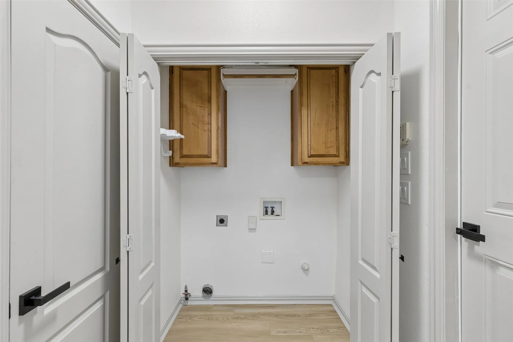 Dedicated laundry area featuring wood-finish flooring, white walls, and wood cabinetry