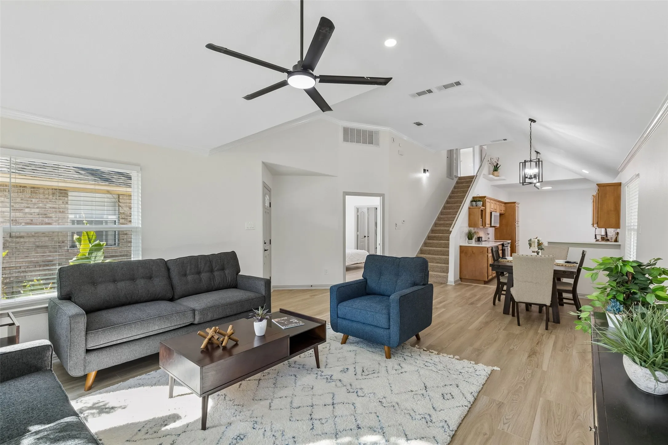 Open-concept living space featuring vaulted ceilings, wood-finish flooring, a modern ceiling fan, and a dining area with pendant lighting
