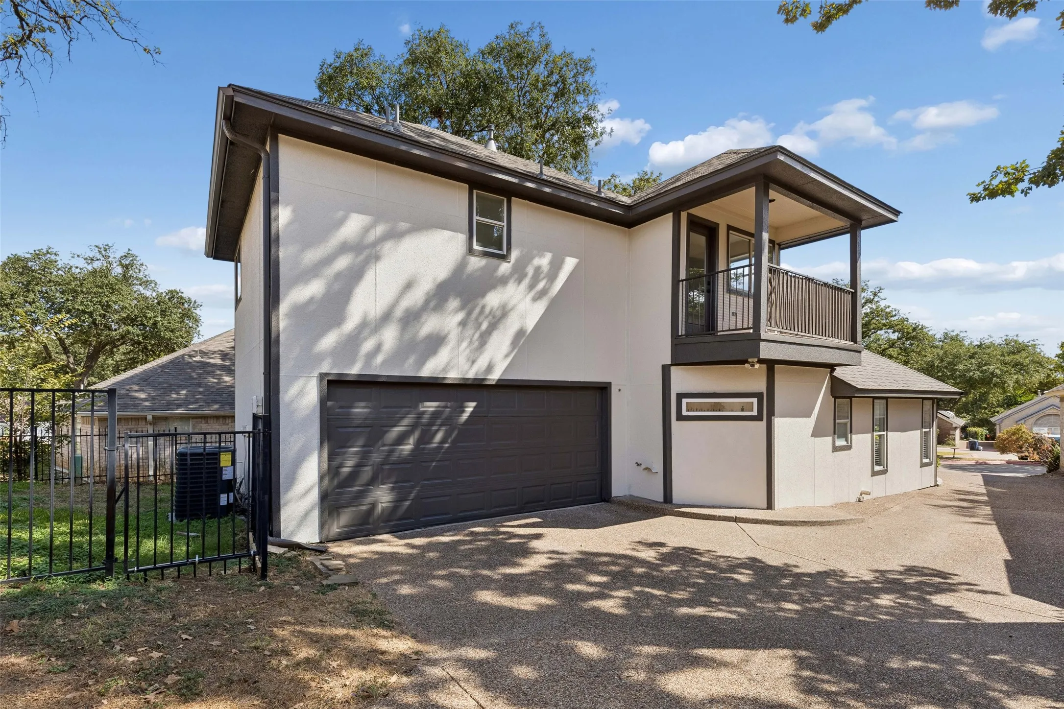 Stucco exterior with a balcony, dark trim, an attached garage, and a wrought iron fence