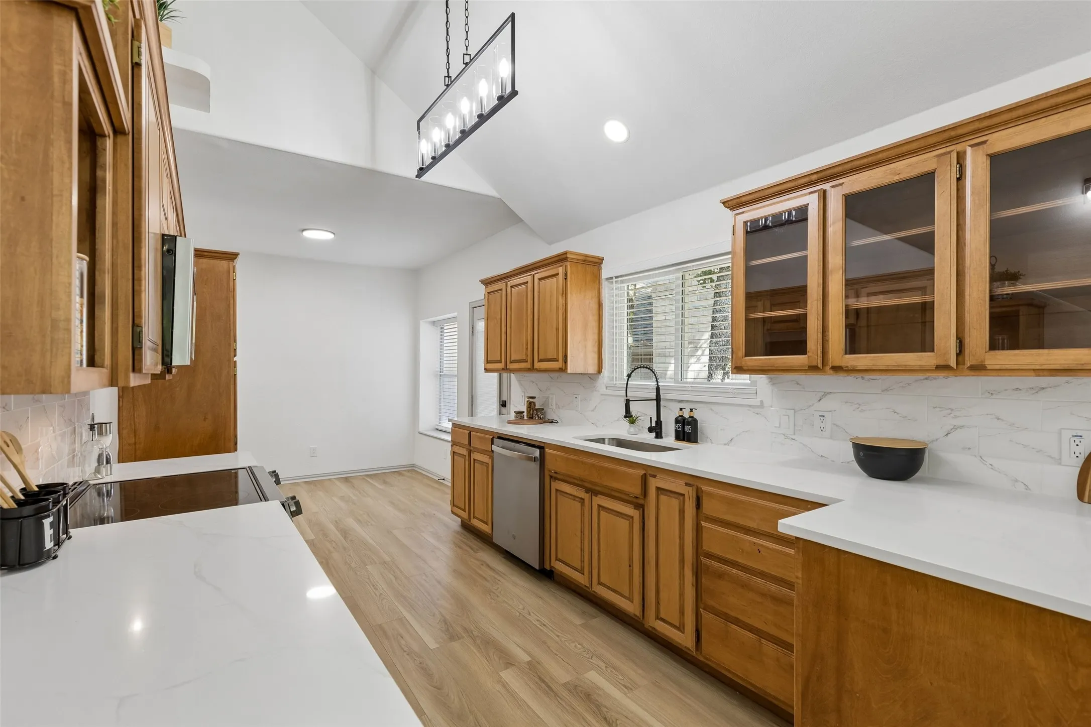 Vaulted ceiling kitchen featuring wood-finish cabinetry, white countertops, and a full tile backsplash