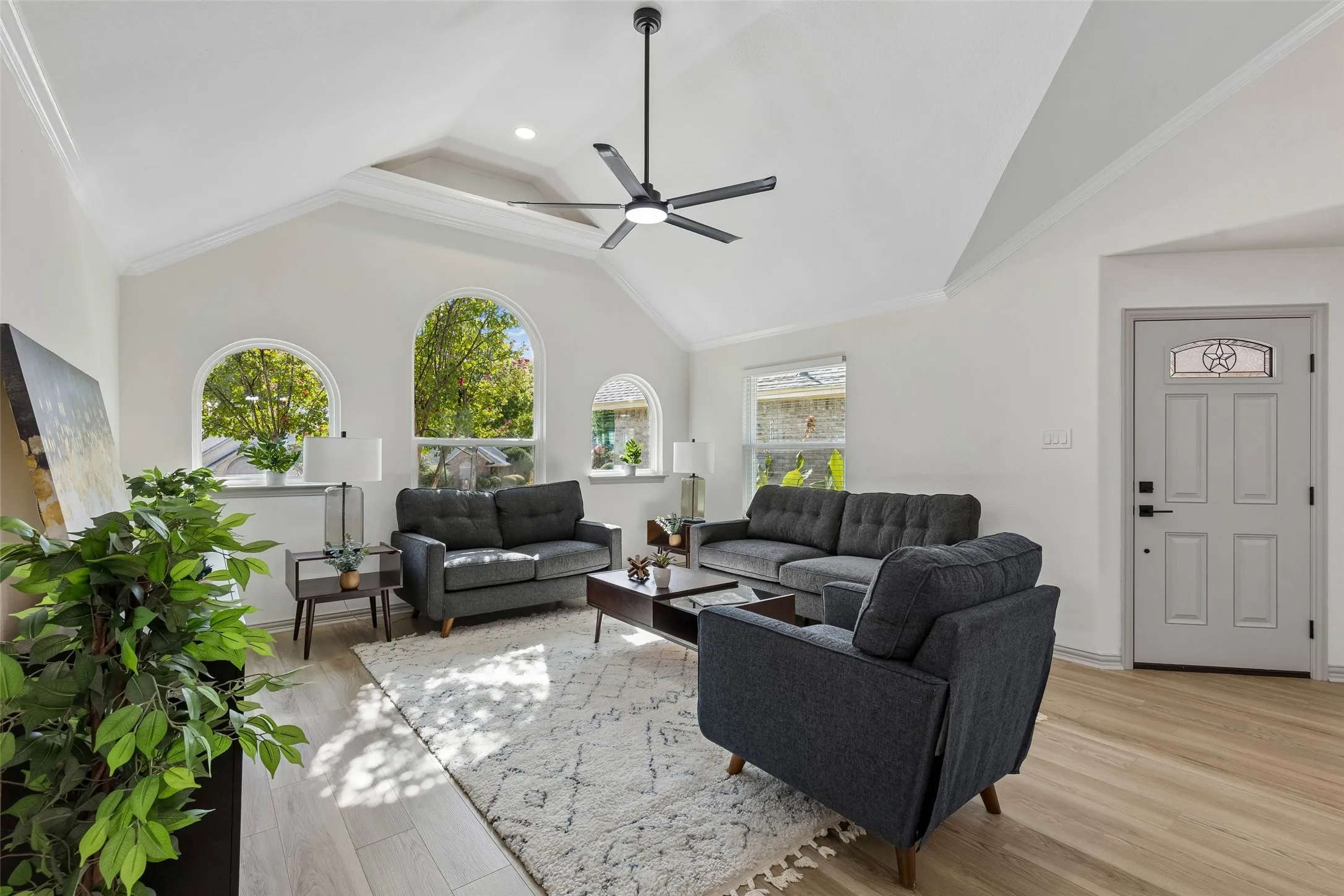 Vaulted ceilings with a ceiling fan, three arched windows, wood-finish flooring, and a paneled entry door with decorative glass