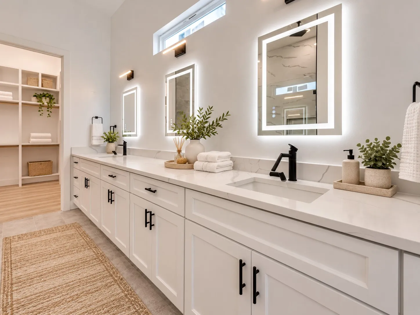 Dual vanity with white cabinetry, matte black hardware, integrated sinks, and backlit mirrors