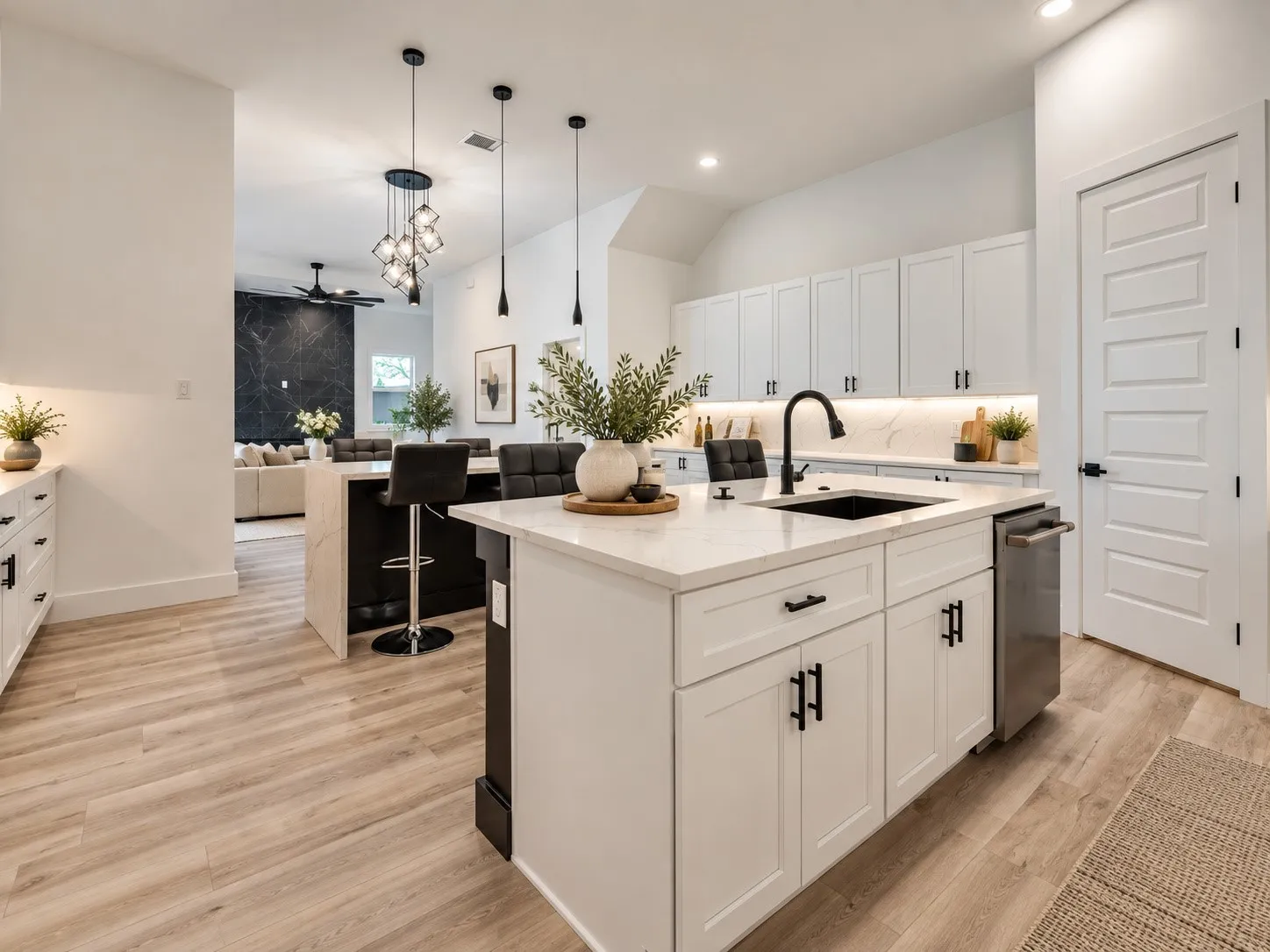 Open-concept kitchen with white cabinetry, wood-finish flooring, and a large island featuring an integrated sink