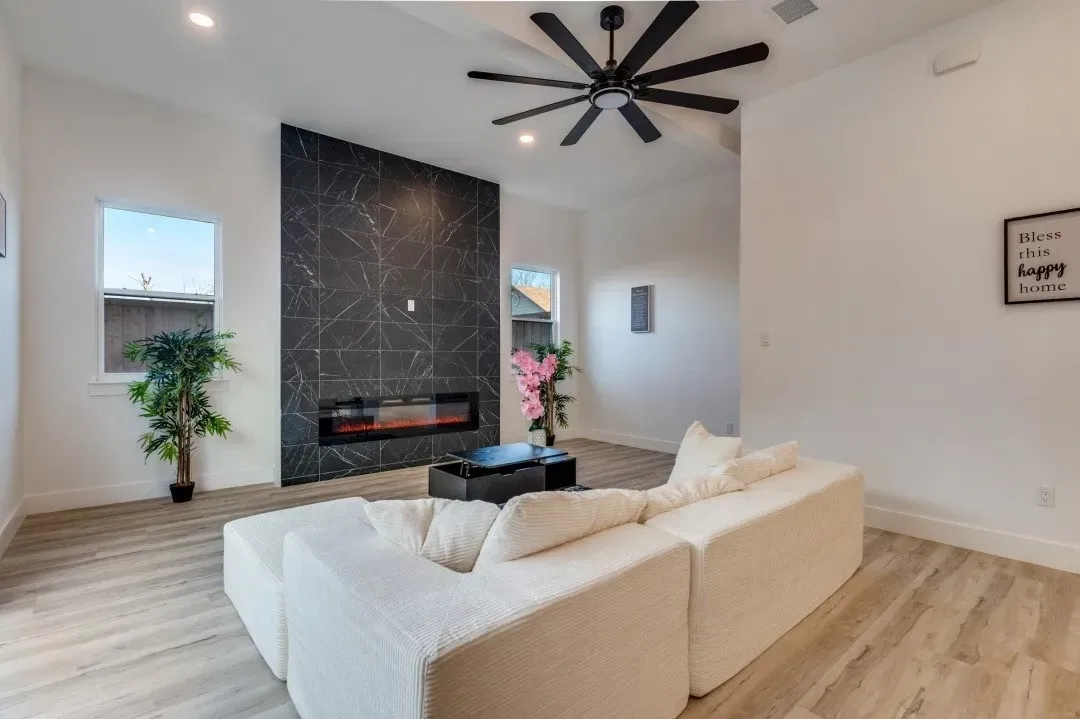 Vaulted ceilings, a black accent wall with an electric fireplace, wood-finish flooring, a black ceiling fan, and recessed lighting
