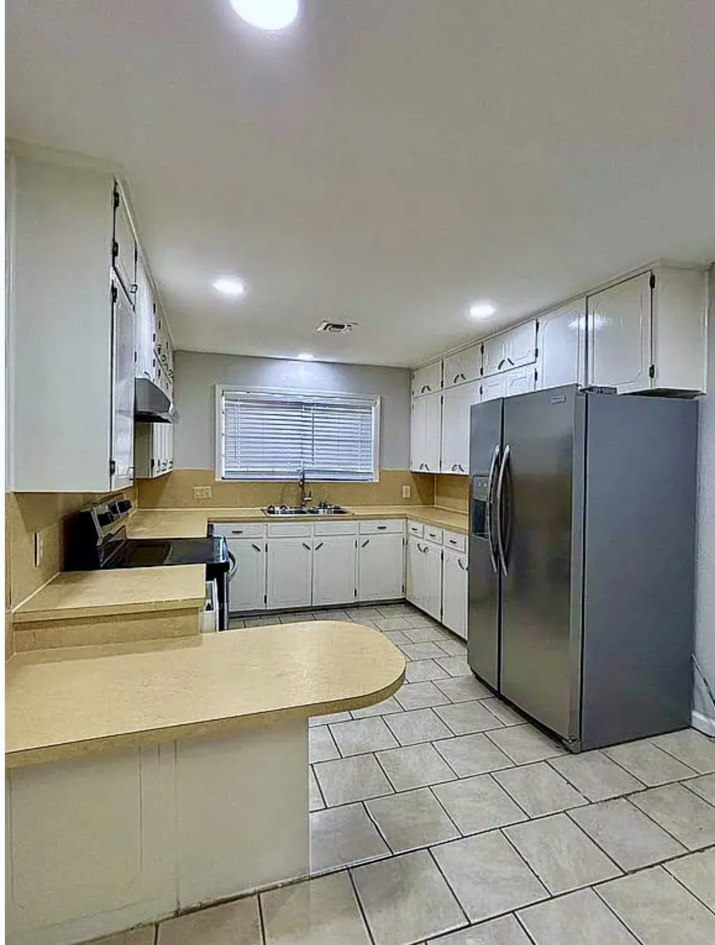 Kitchen featuring light-toned tile flooring, white cabinetry, a double-basin stainless steel sink, and light-toned countertops
