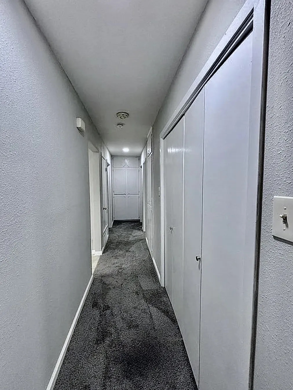 Hallway featuring grey carpeting, light grey walls, and built-in closet doors