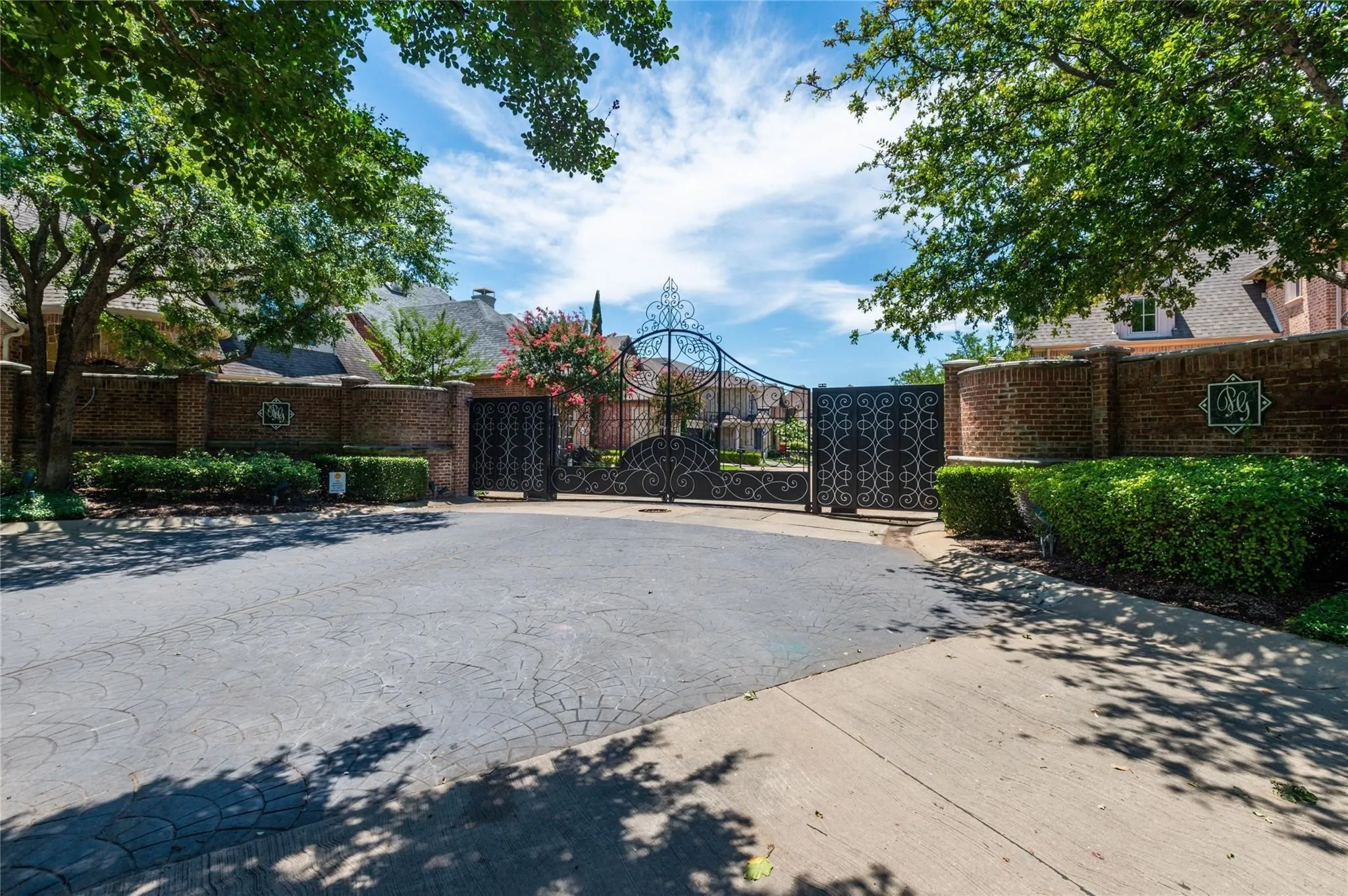 Ornate wrought iron gate with brick pillars, brick privacy wall, and mature landscaping