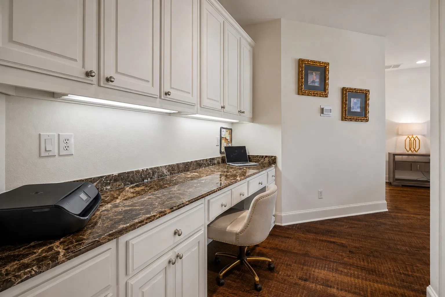 Built-in desk featuring a stone-look countertop, under-cabinet lighting, extensive upper and lower cabinetry, and wood-finish flooring
