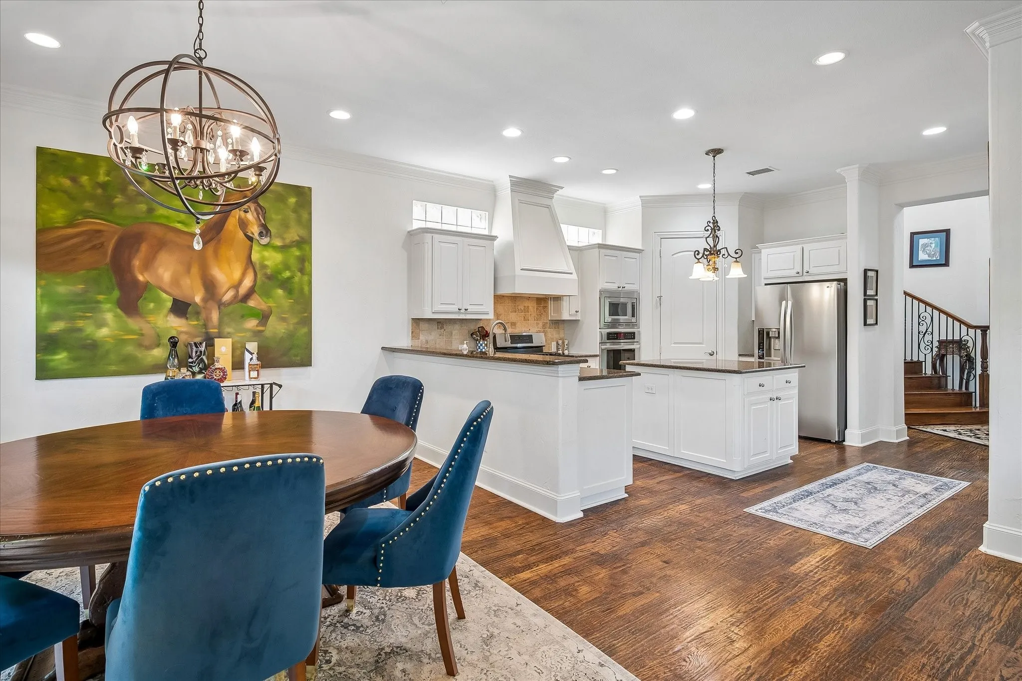 Hardwood-style flooring throughout, white cabinetry, stainless steel appliances, kitchen island with counter seating, and recessed lighting