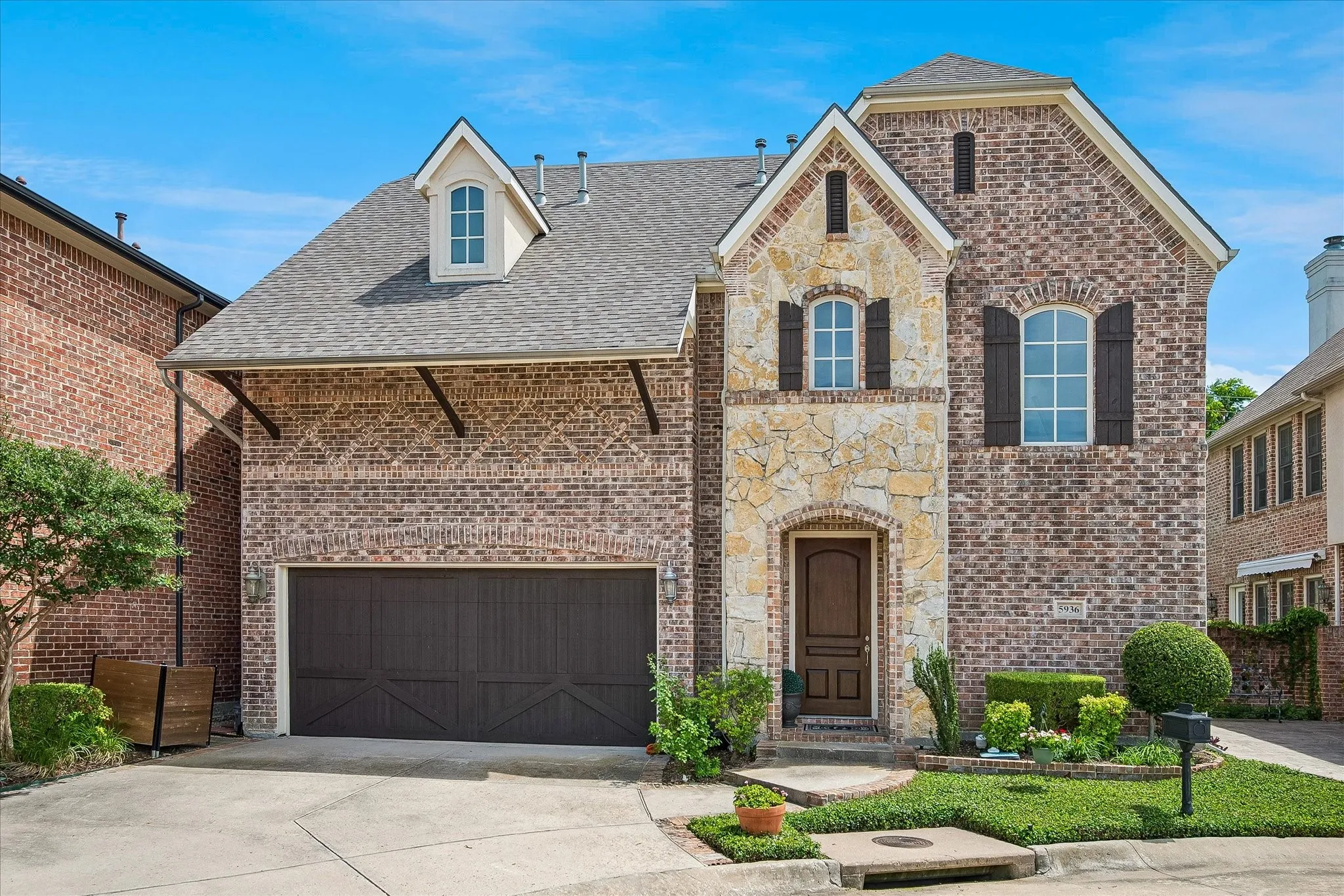 Brick and stone-veneer exterior with a prominent dormer window, an arched entryway, and a two-car garage
