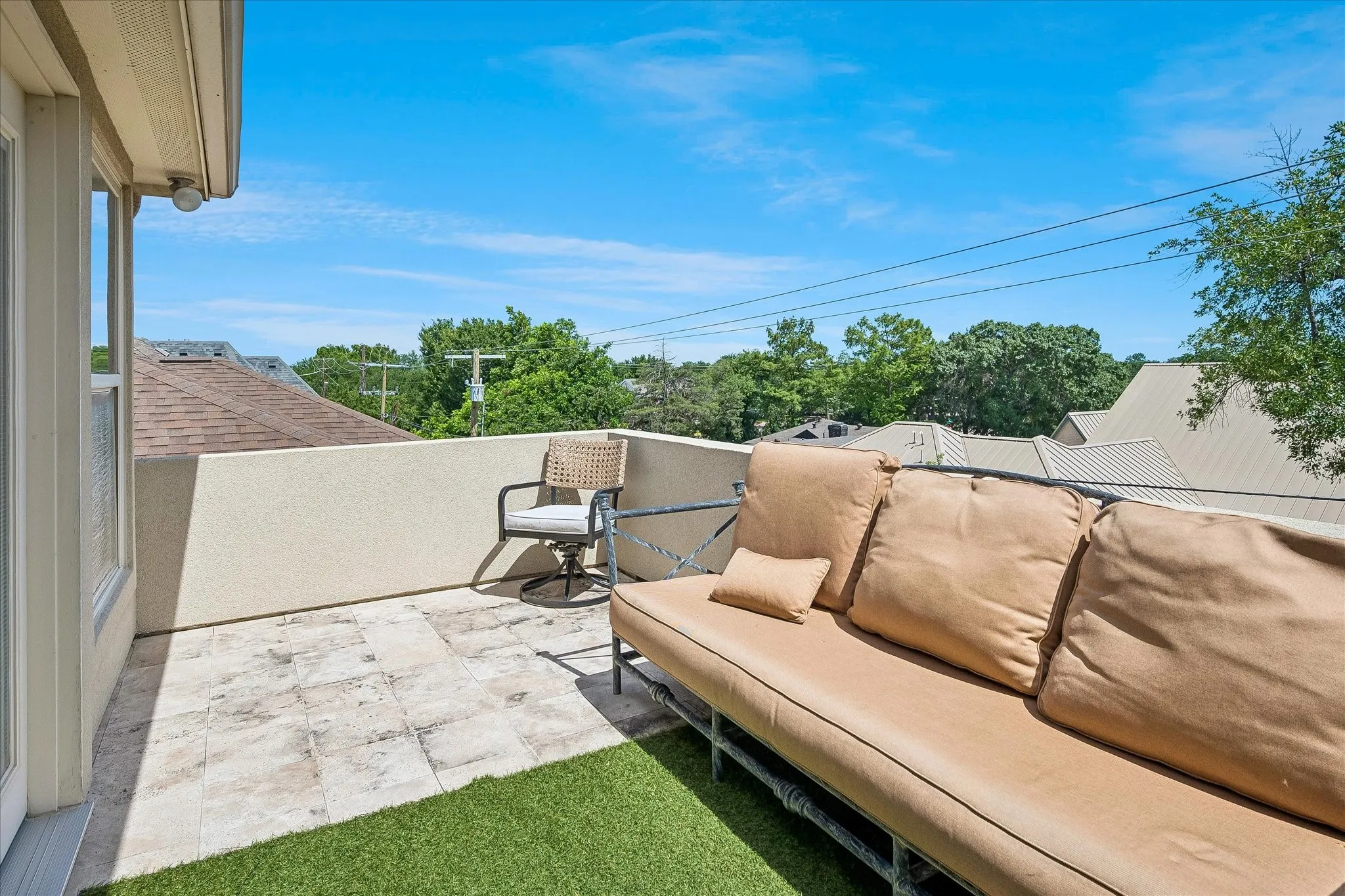 Outdoor balcony with a tiled surface and partial artificial turf, featuring a stucco-finished privacy wall