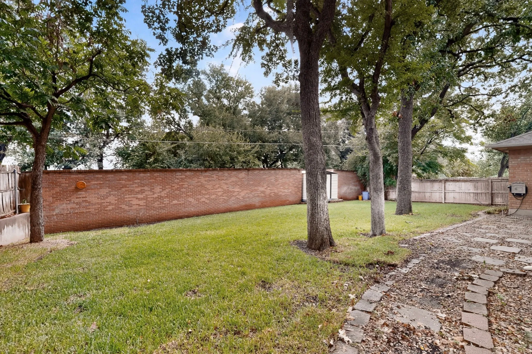 Expansive backyard featuring a manicured lawn, mature trees, and a brick privacy wall