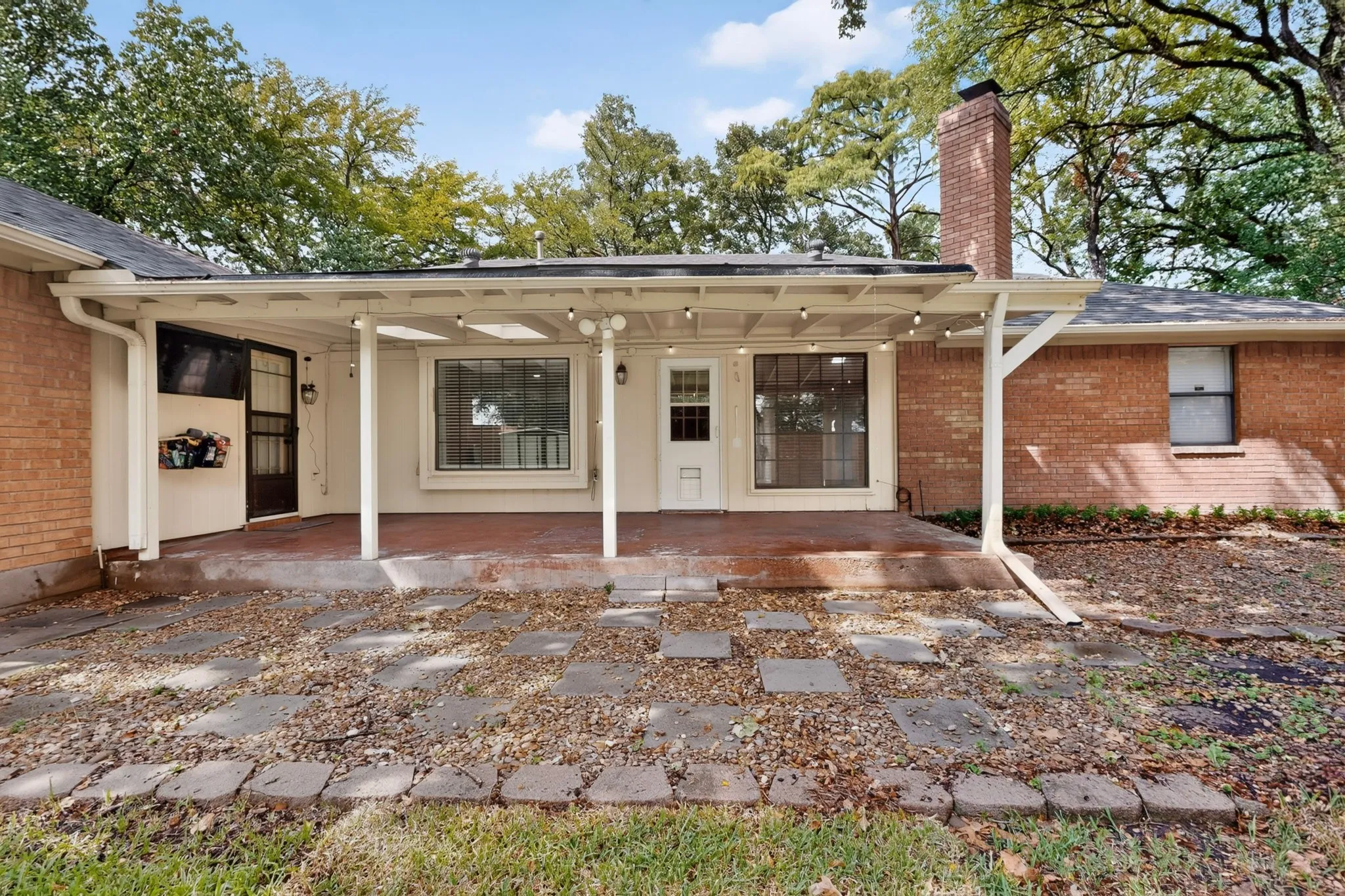 Covered patio with string lighting, brick exterior, and a stone-paver walkway