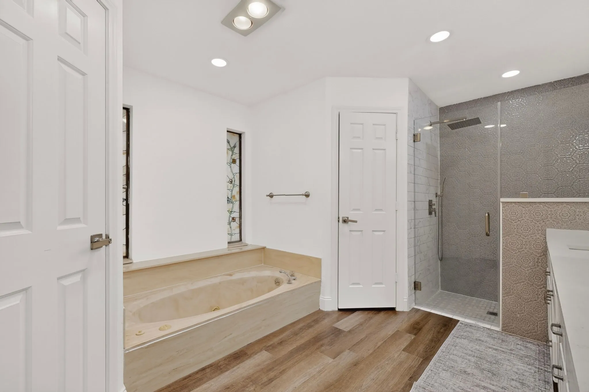 Walk-in shower with glass enclosure, soaking tub with tiled surround, wood-finish flooring, and recessed lighting