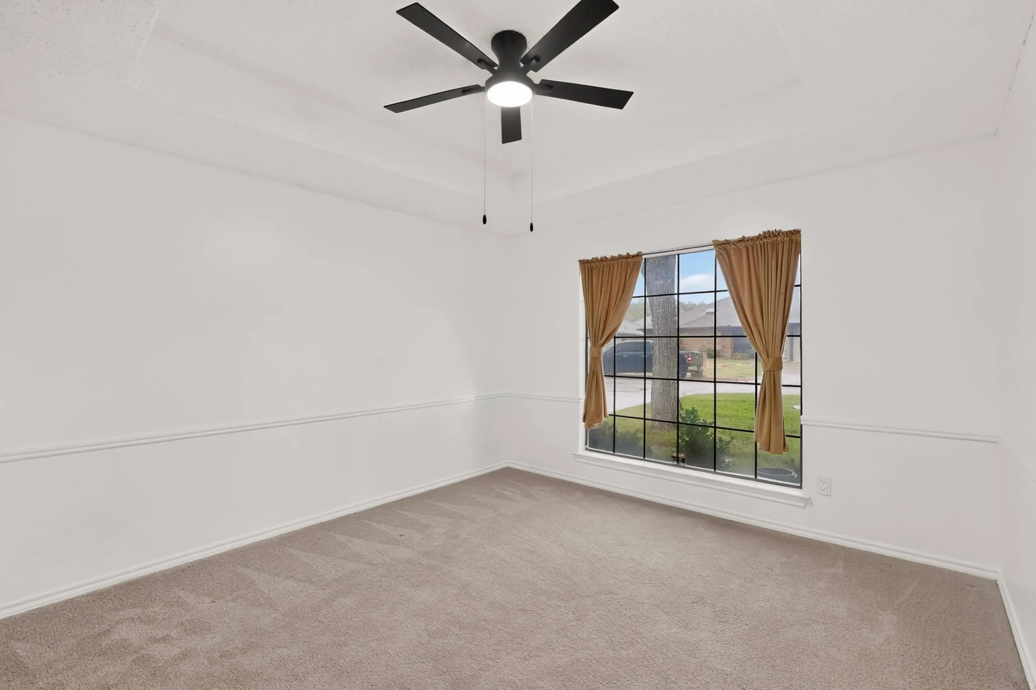 Tray ceiling with a ceiling fan, large window with grid pattern, and neutral carpeting