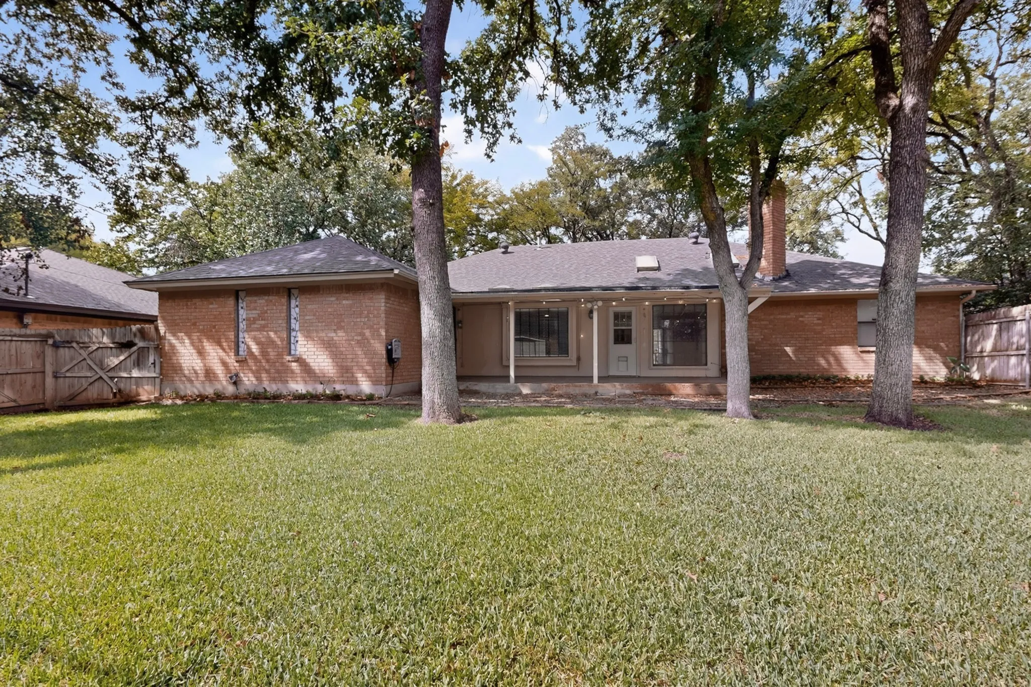 Expansive backyard with a brick exterior, covered patio, and mature trees